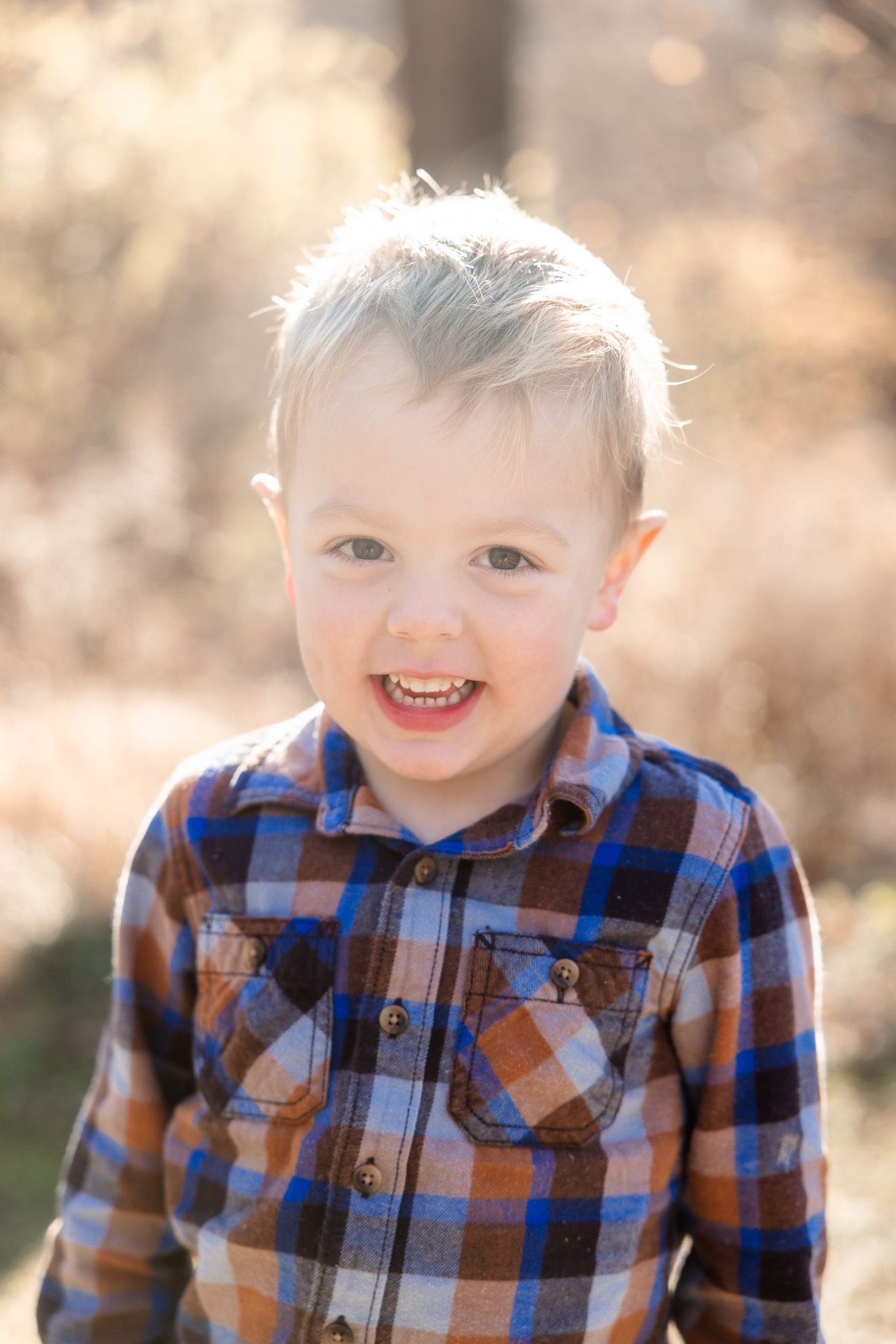 Toddler in plaid shirt smiling during golden hour outdoor photoshoot.