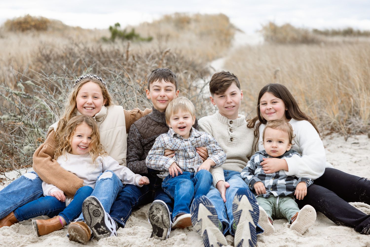 Siblings lounging together on sandy ground with tall grass in background.