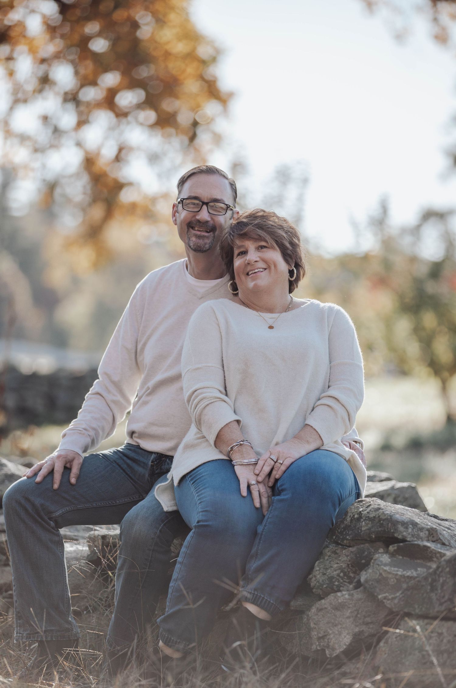 A couple sits together on rocky terrain during a warm autumn day.