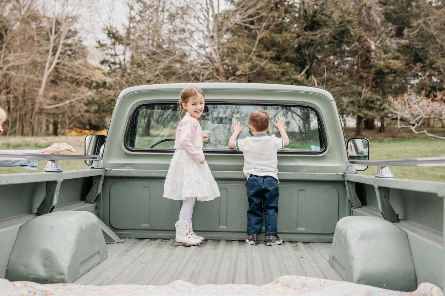 Two young children standing in the bed of a vintage green pickup truck outdoors.