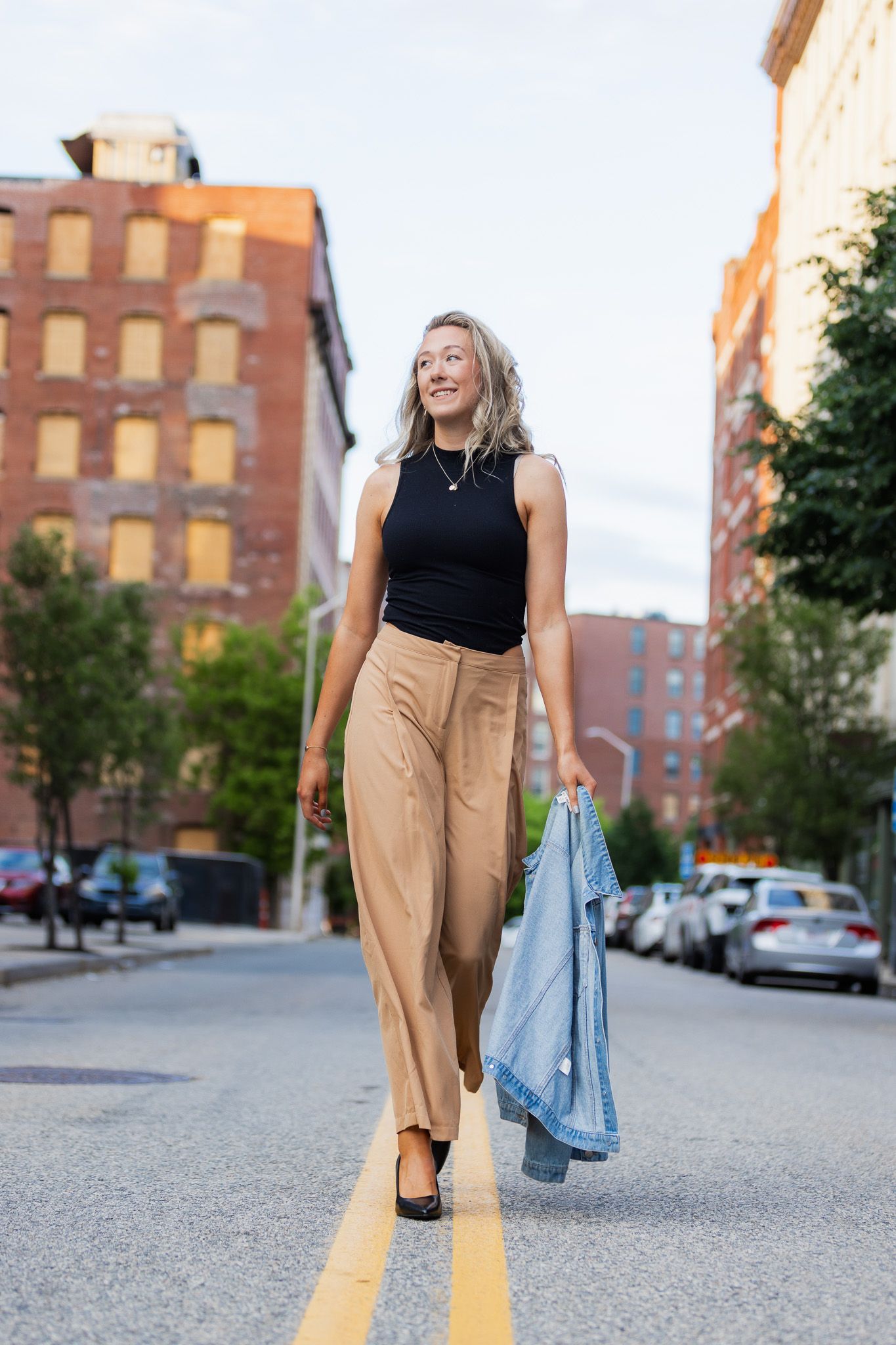 Casual street fashion photo with person walking in tan pants and black top near brick buildings.