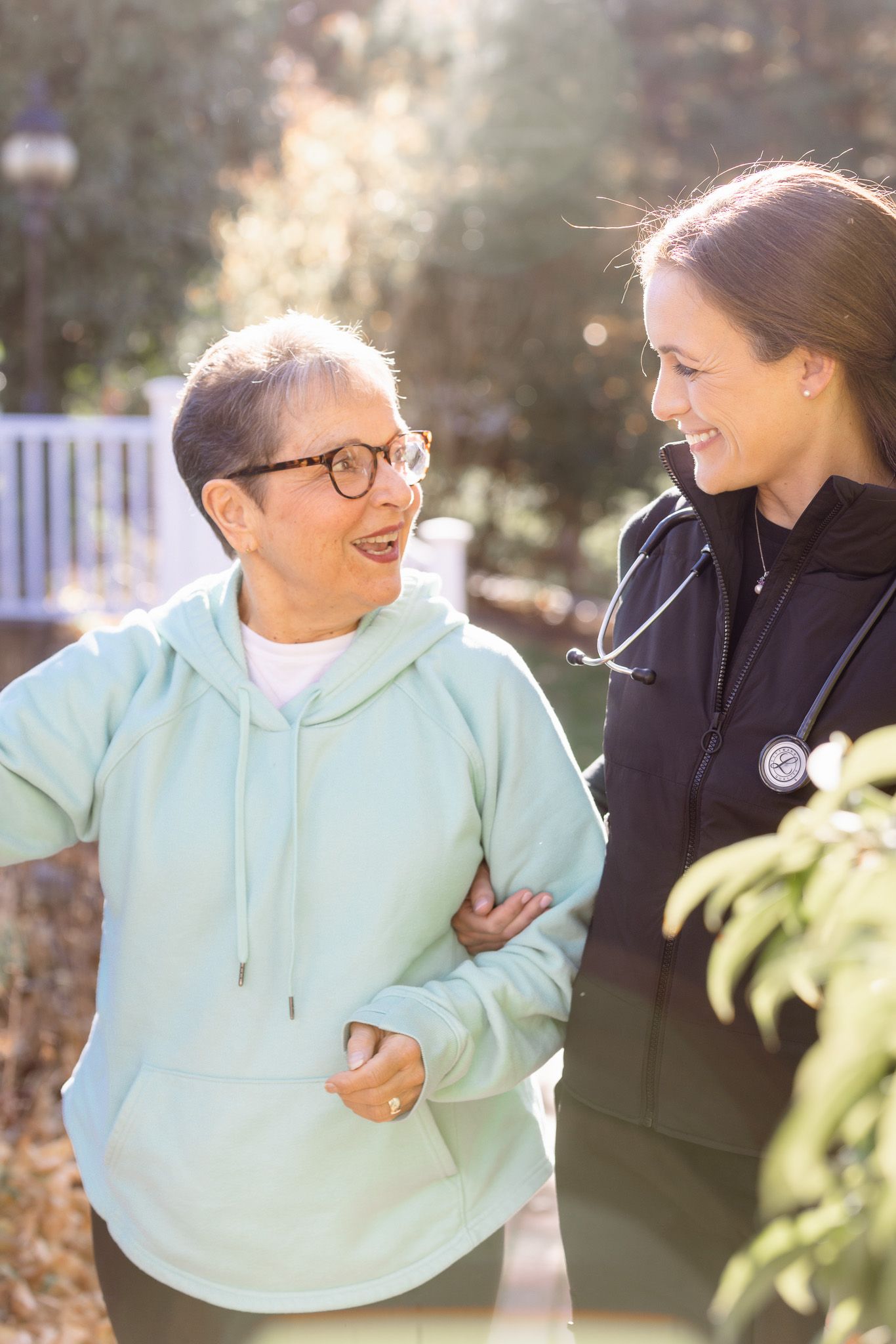 Two people in casual outdoor wear share a joyful moment while walking together in a sunlit garden setting.
