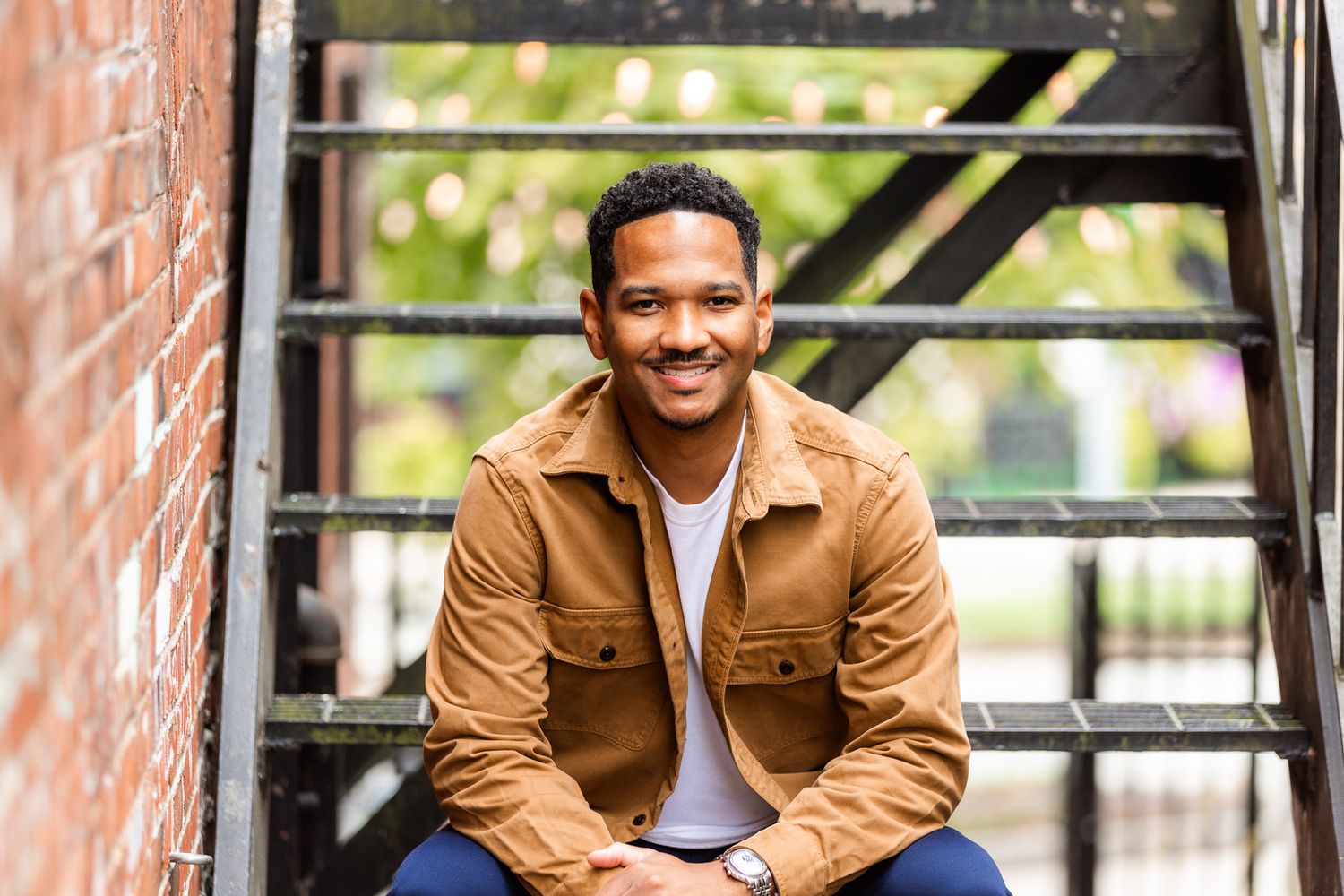 Professional portrait session in casual brown jacket against brick wall background.