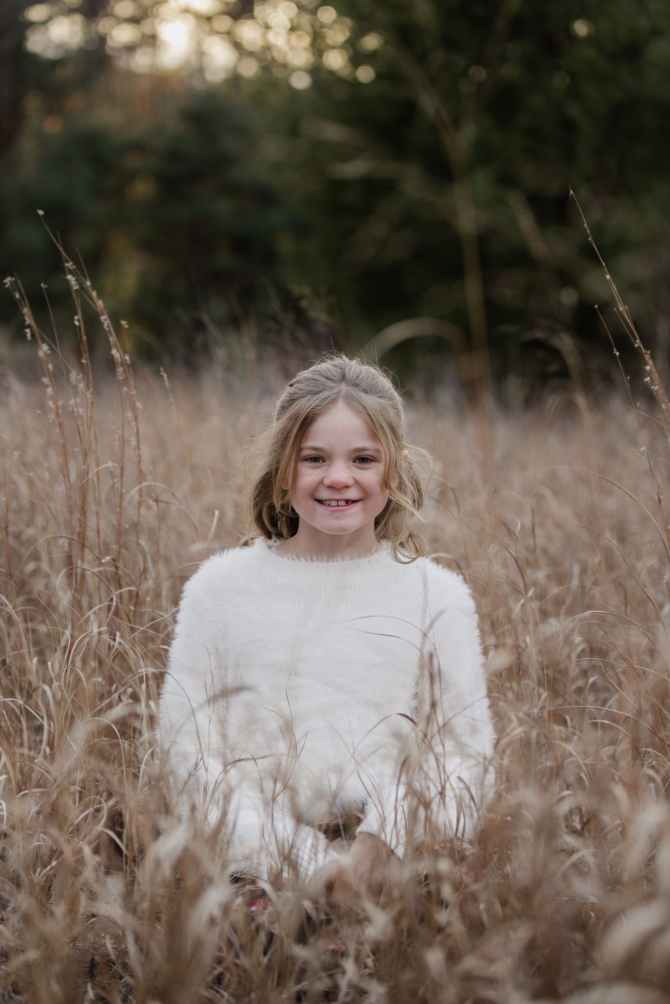 Person in white sweater sits among tall golden grass during sunset.