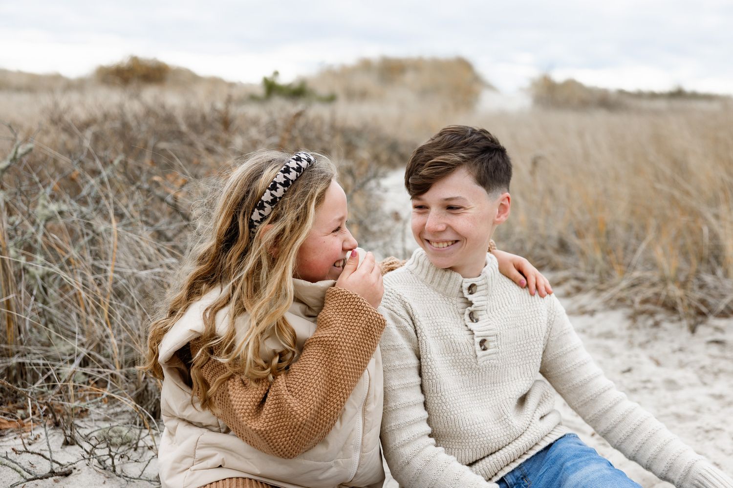 A romantic couple sits together on a sunny winter day outdoors wearing cozy sweaters.