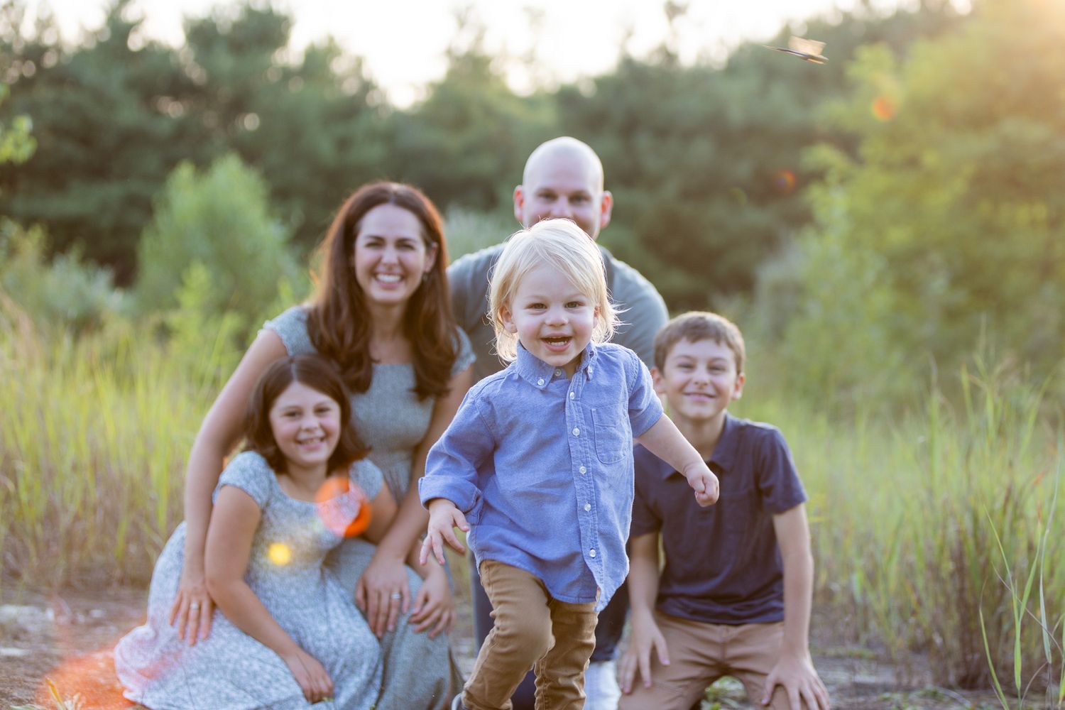 Family laughs together during casual outdoor photo session in grassy field.