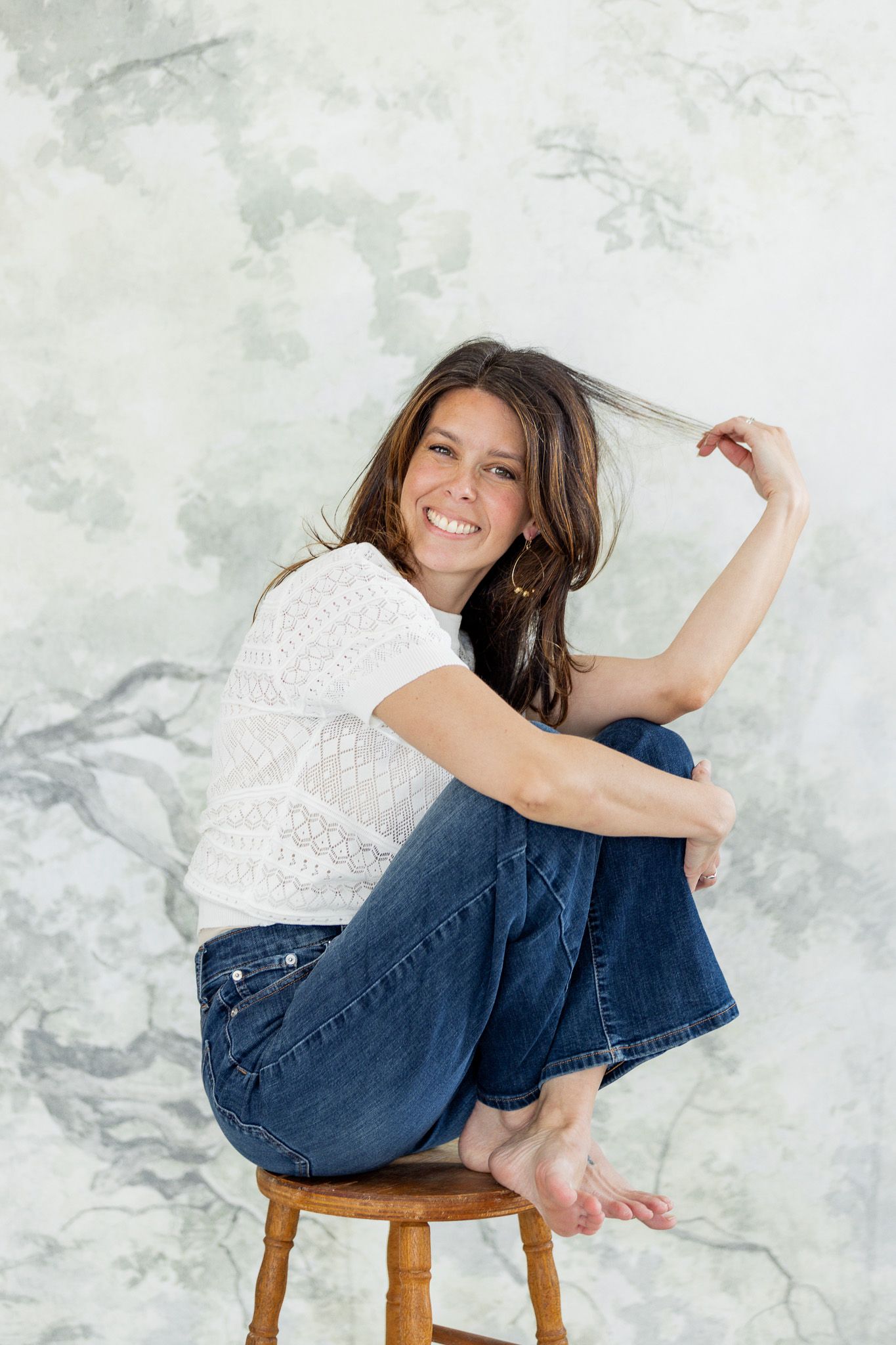 Casual lifestyle portraits on wooden stool wearing white top and denim.