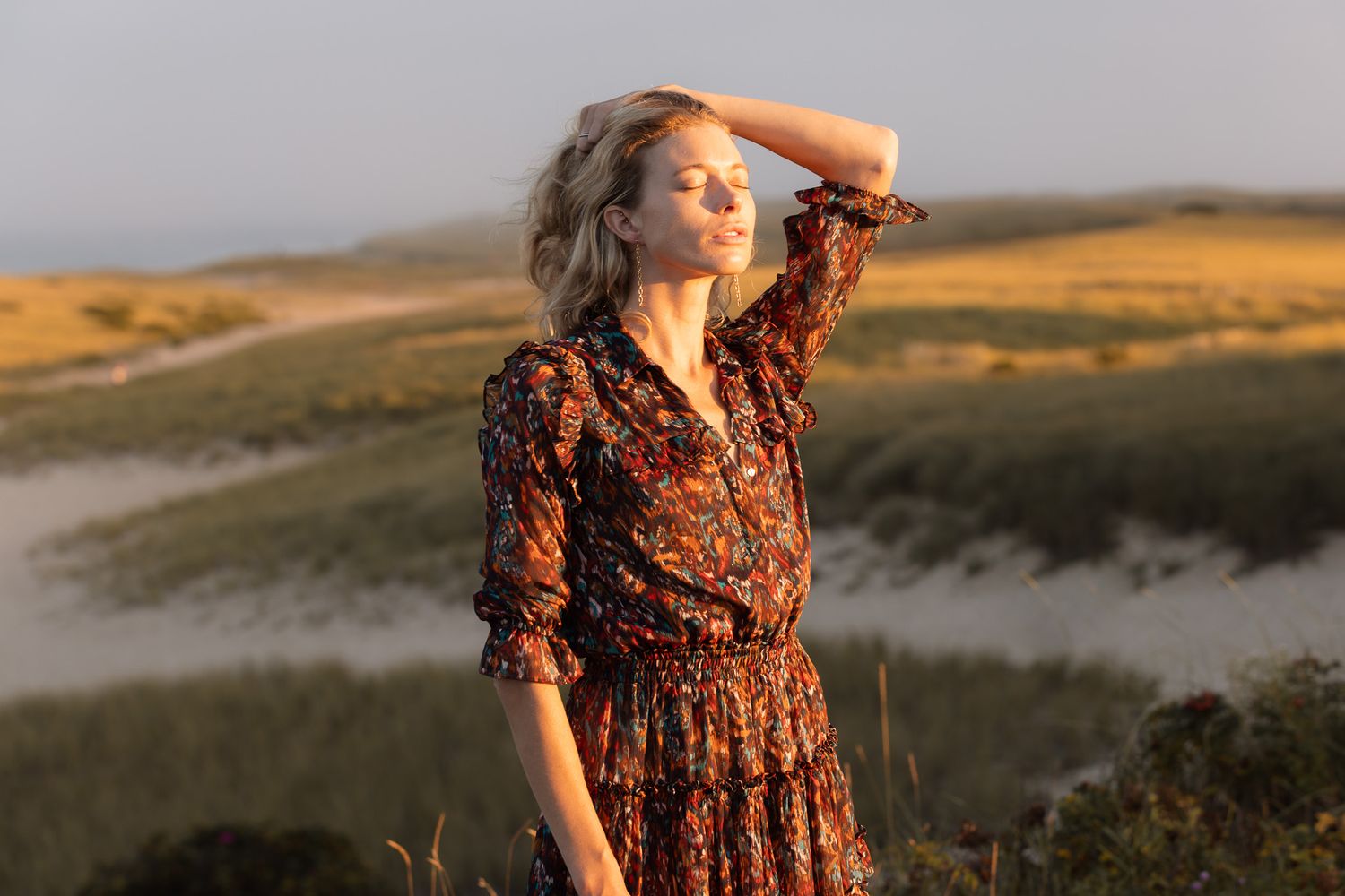A floral dress photographed in golden sunset lighting against a scenic outdoor landscape.
