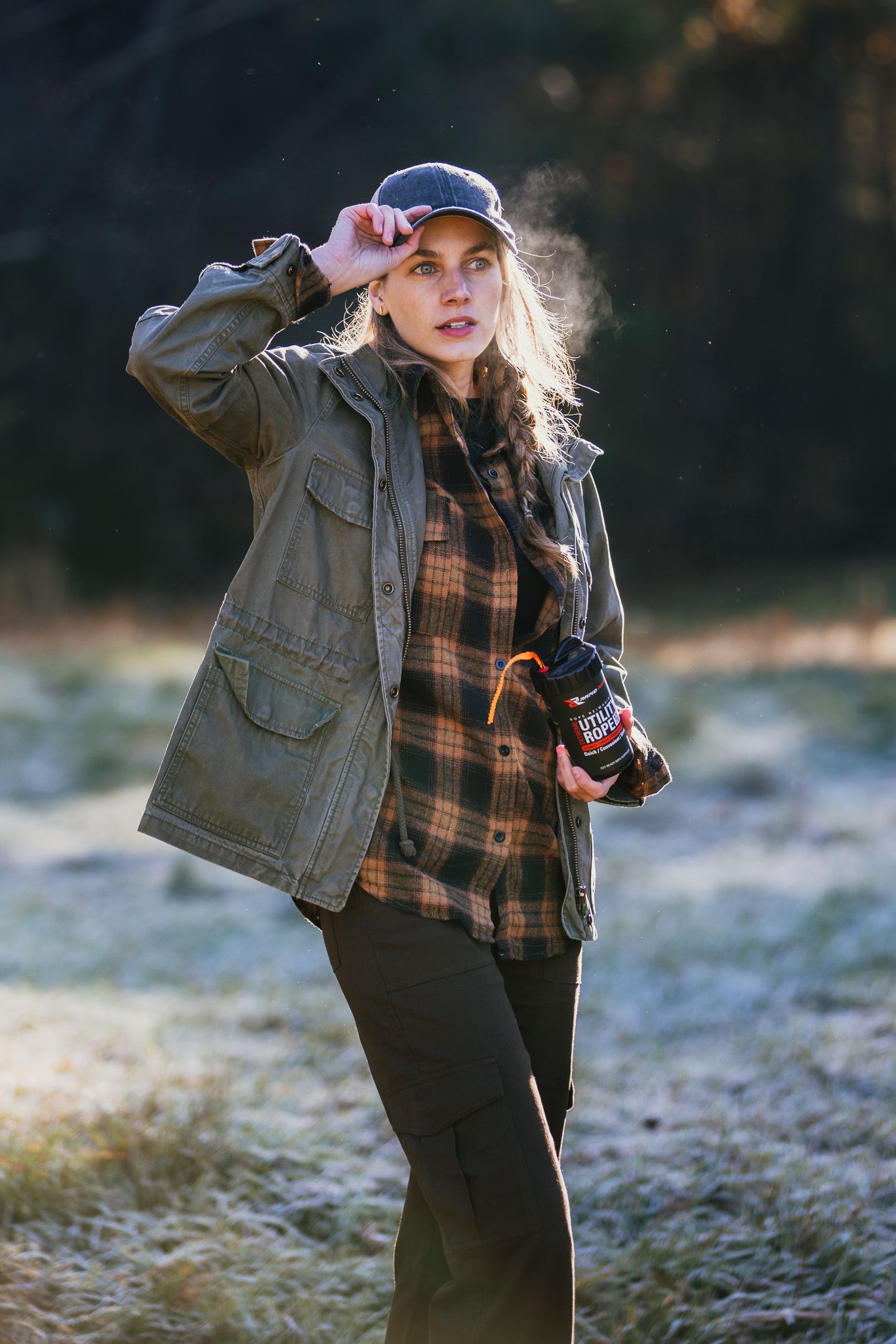 Person in denim jacket and baseball cap posing outdoors in winter landscape.