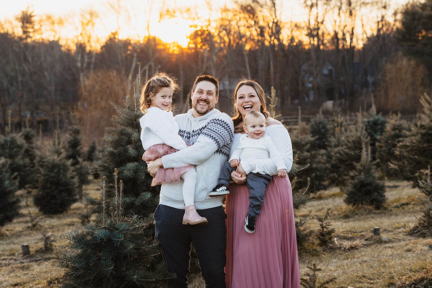 Family embracing outdoors at sunset with evergreen trees in background.