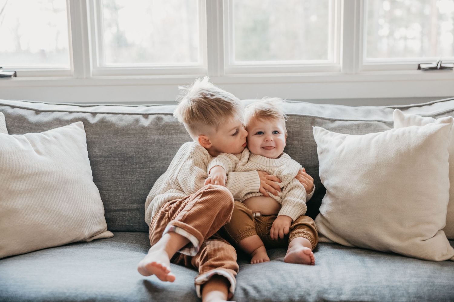 Siblings in coordinating outfits play together on comfortable gray sofa.