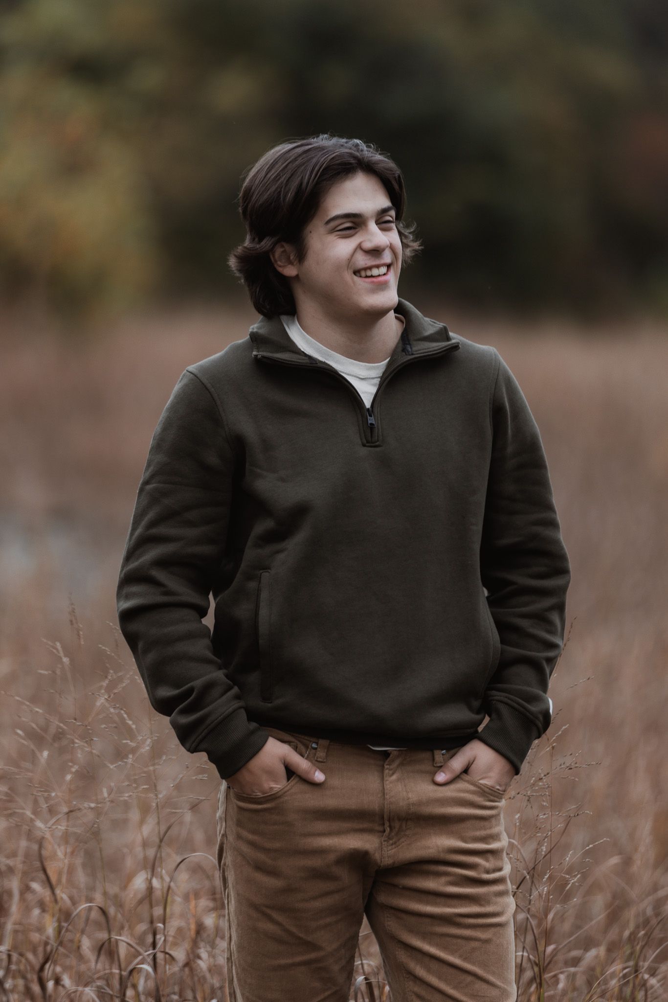 Person in dark hoodie and brown pants stands in tall grass during golden hour.