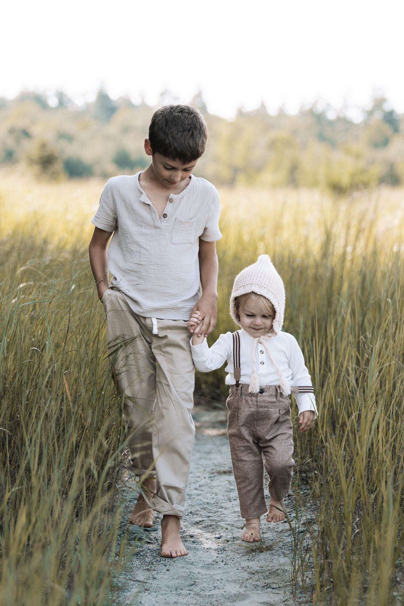 Two people walking together through a path in tall grass field.
