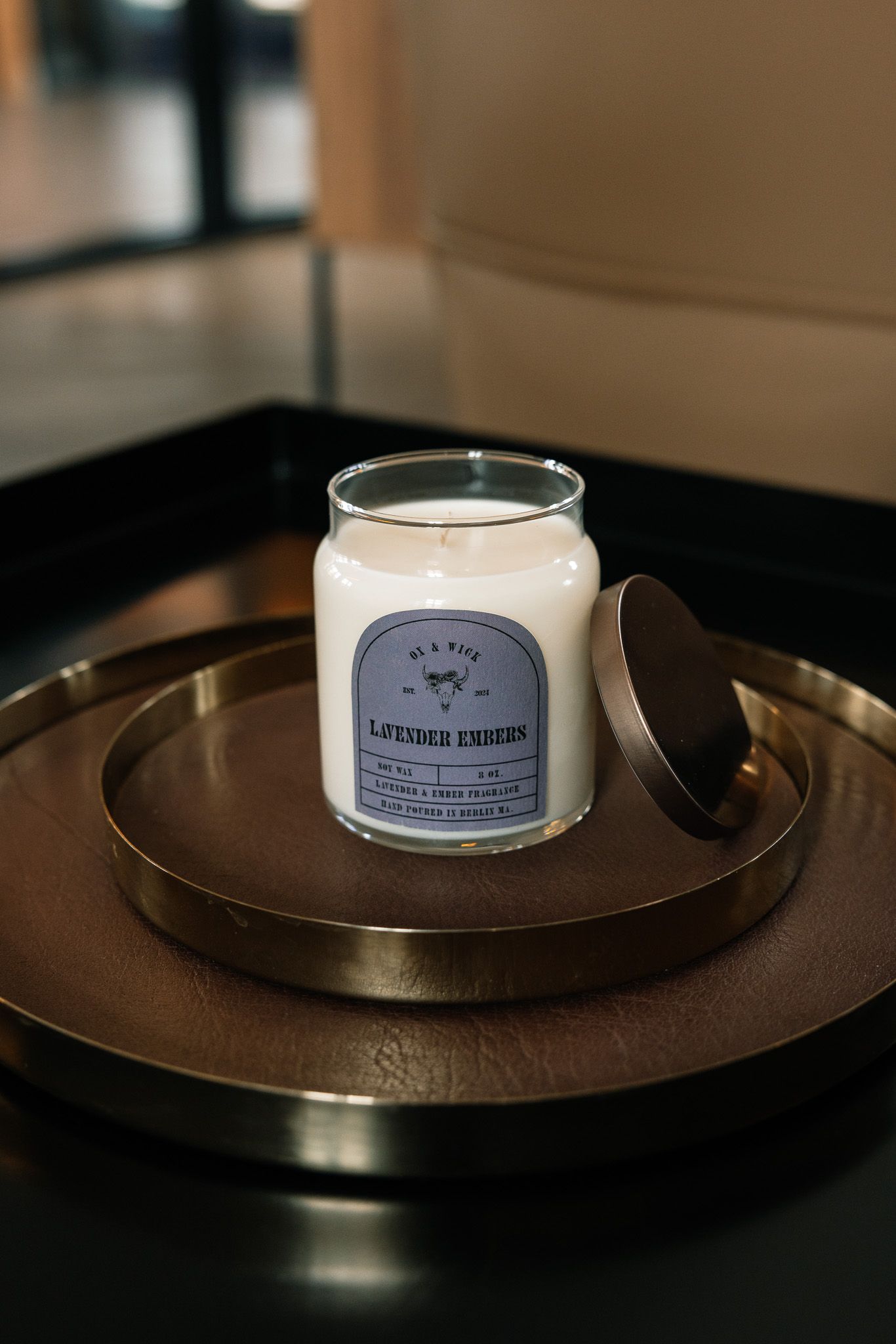 Scented candle displayed on a dark circular metal plate with moody lighting.