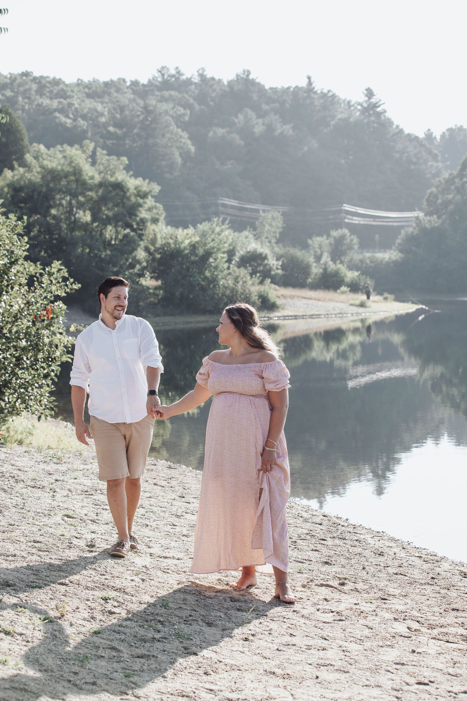 A couple walks hand in hand along a serene lakeside path on a sunny summer day.