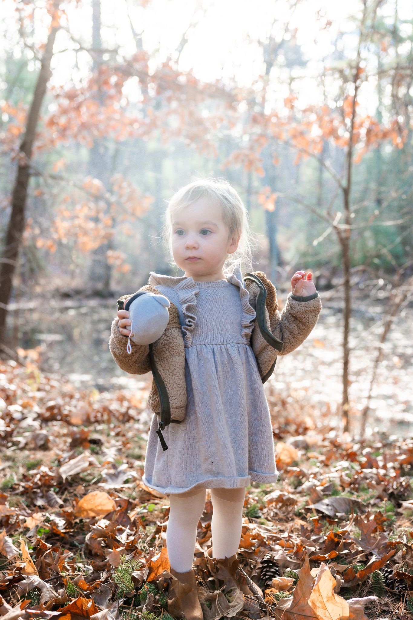 Small child exploring fallen autumn leaves wearing a gray dress and brown cardigan.