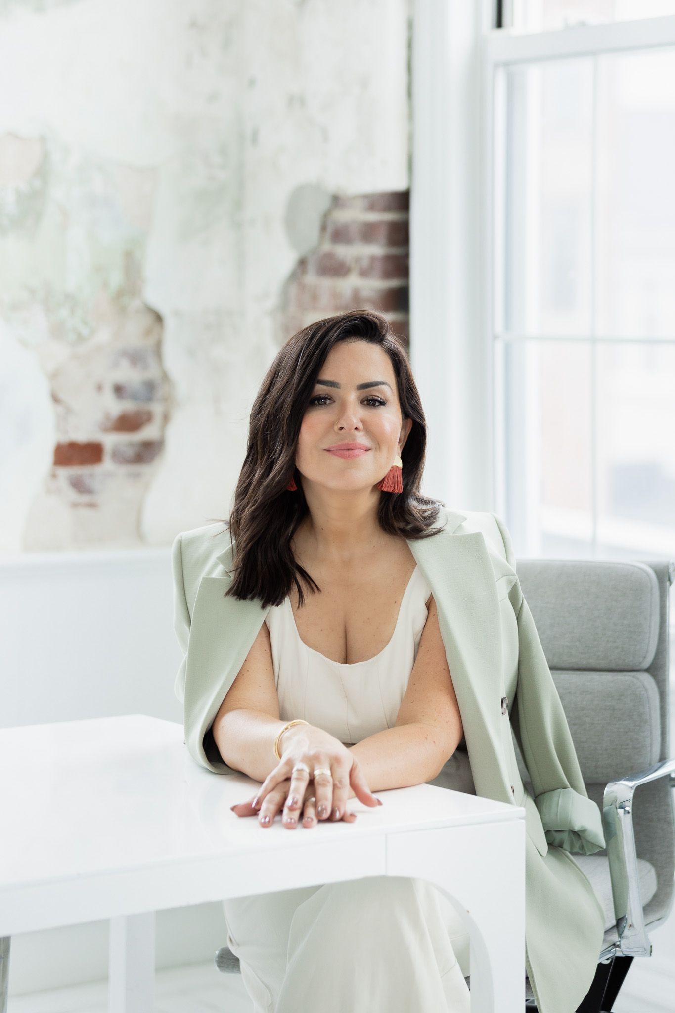 Professional branding photos in mint blazer at white desk with exposed brick wall background.