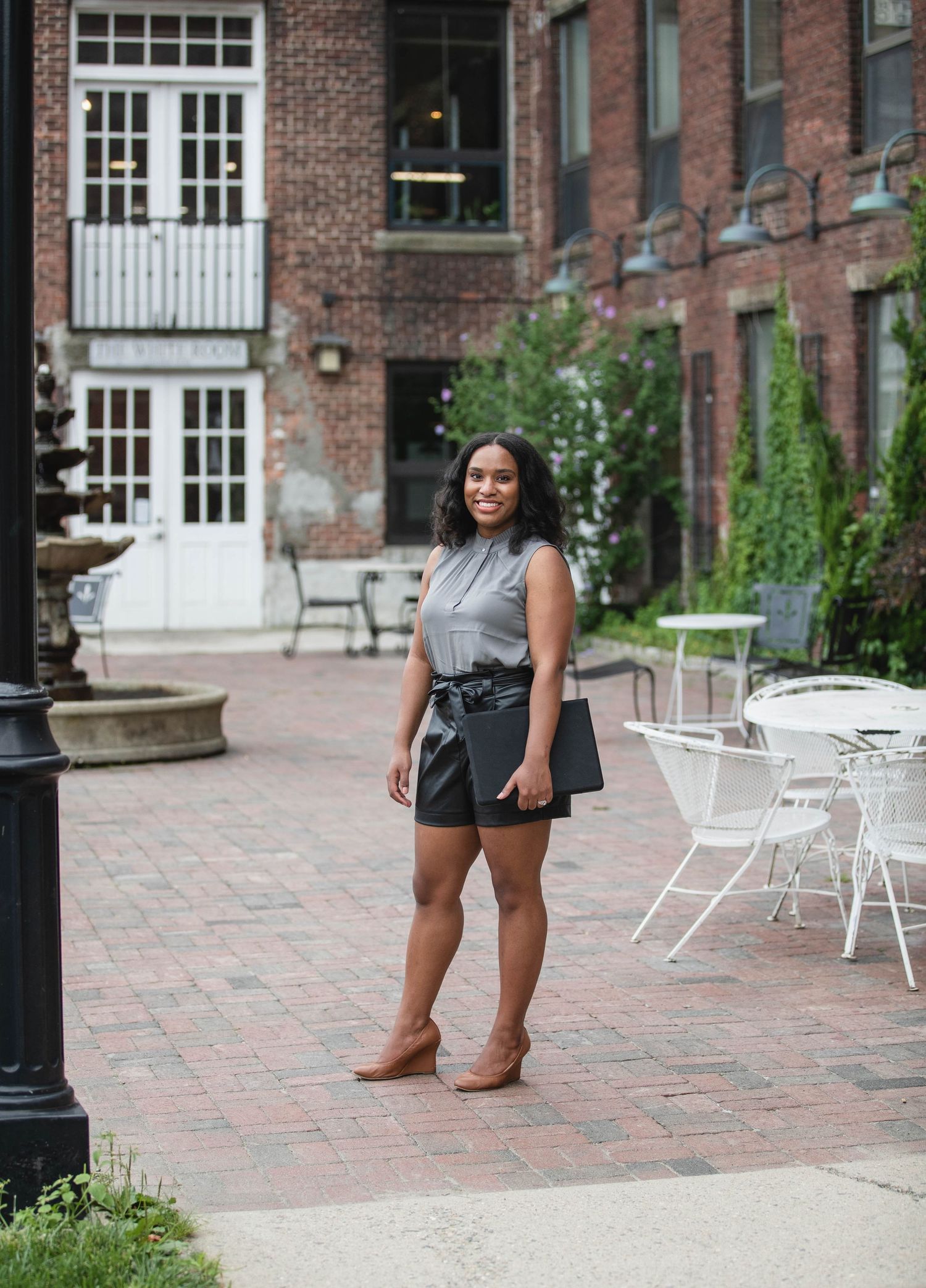 Urban fashion photography at brick building courtyard with outdoor furniture and cobblestone pavement.
