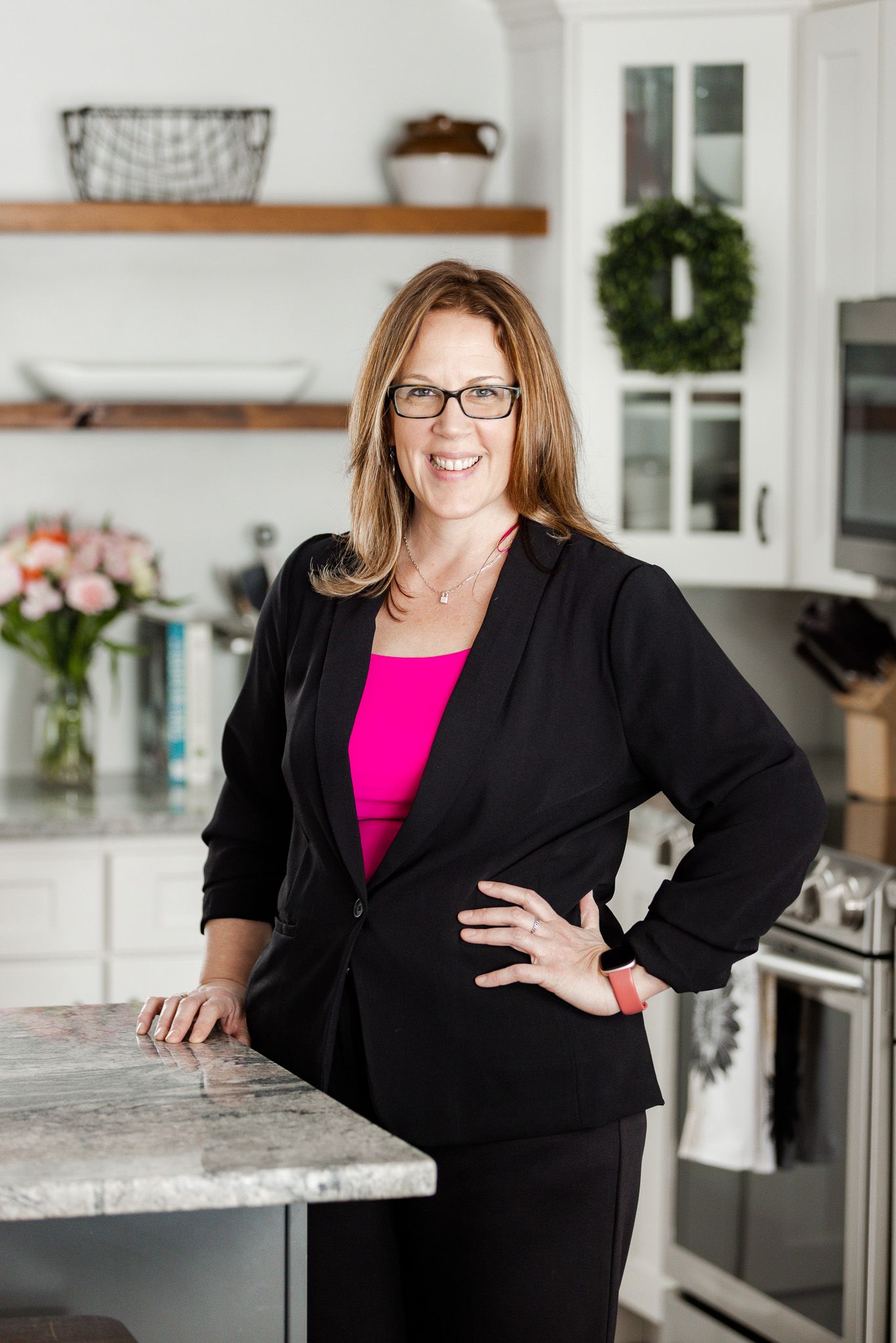 Professional headshots in modern kitchen wearing black blazer and pink top.