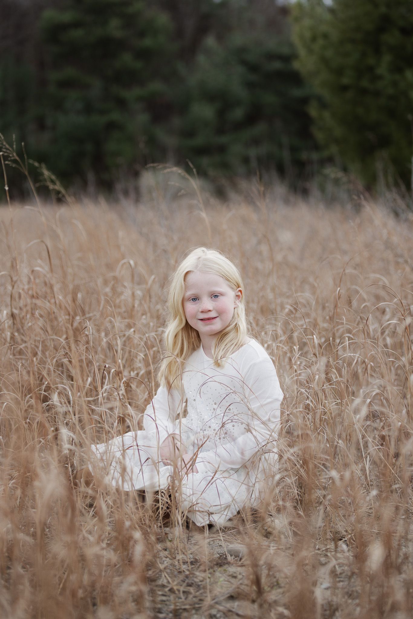 Person wearing white clothing poses in field of tall brown grass during autumn.