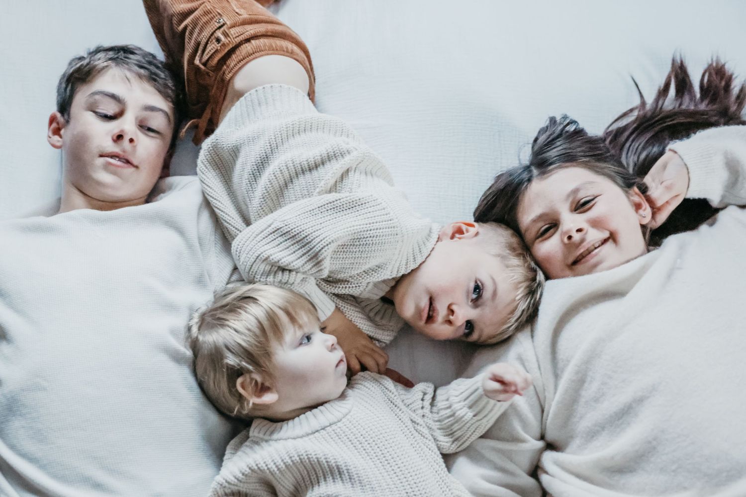 A group of people lying down together on a light colored surface in cozy white sweaters.