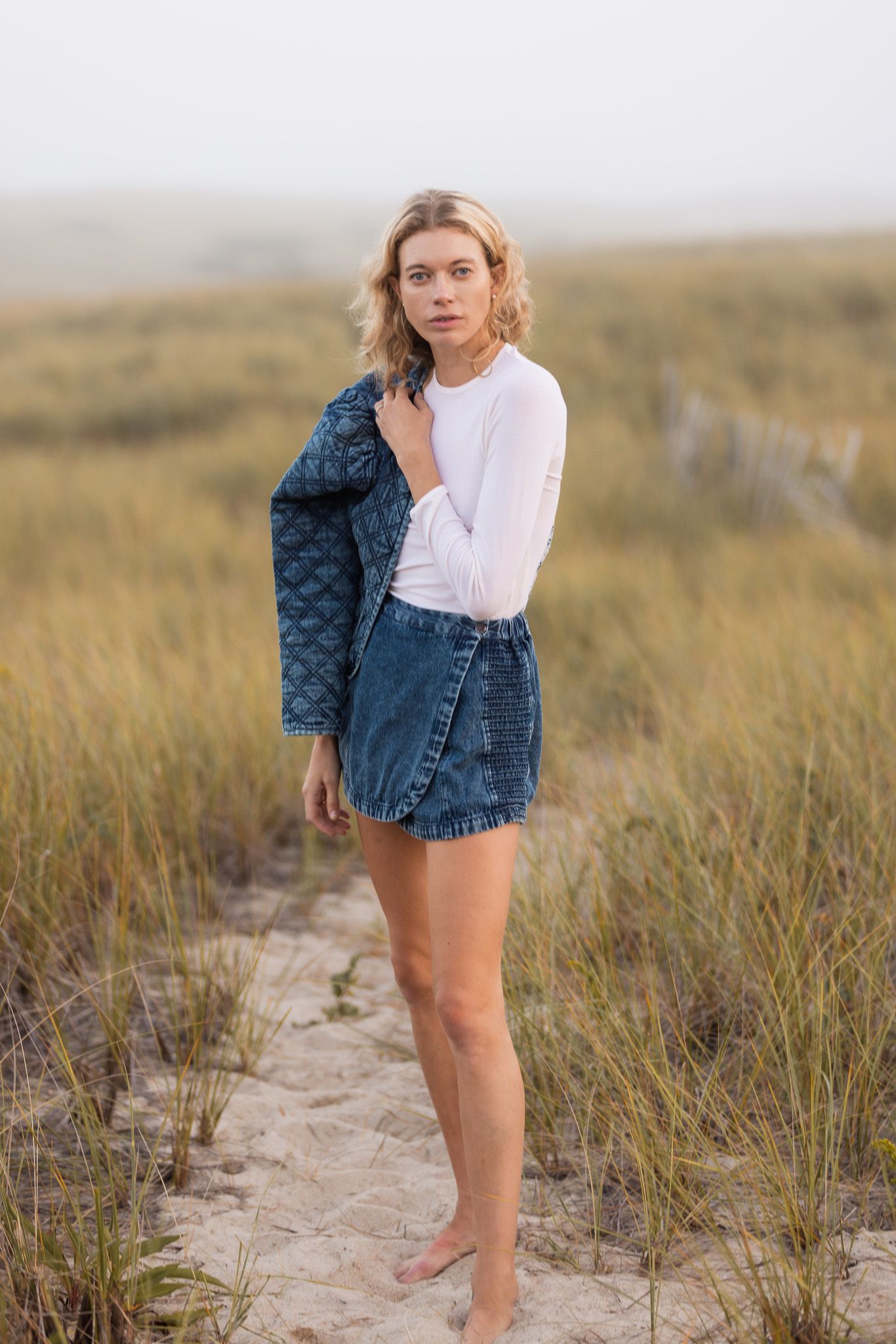 Casual summer outfit featuring denim and white top photographed in beach grass.