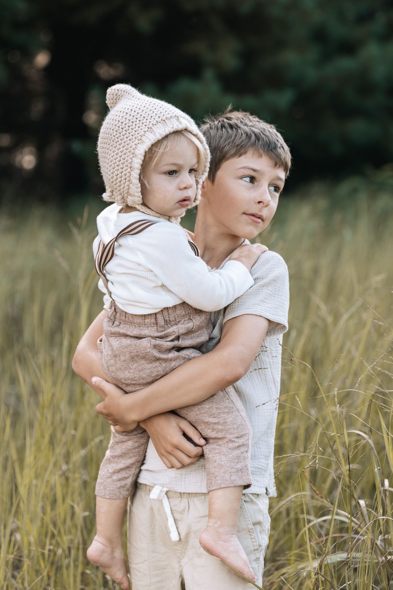 Two siblings share a tender embrace while standing together in a sunlit wheat field on a summer afternoon.