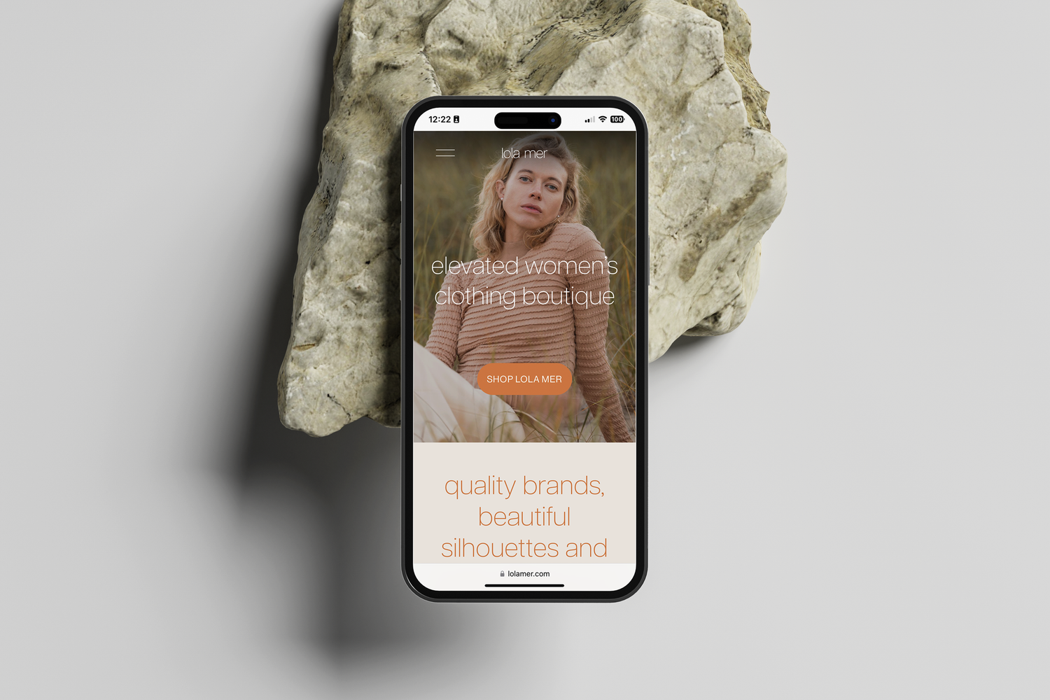 A mobile phone displaying an e-commerce website layout rests against a textured white stone or mineral background.