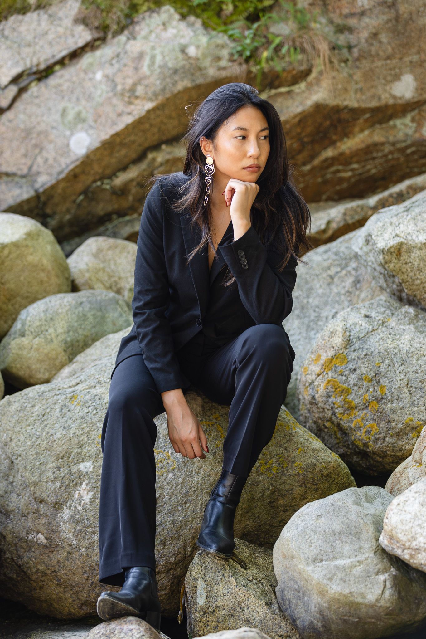 Fashion portraits in a black outfit posed on rocky terrain.