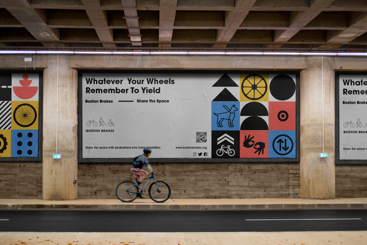 A cyclist rides past a large graphic wall display with colorful geometric shapes and symbols under a concrete overpass.
