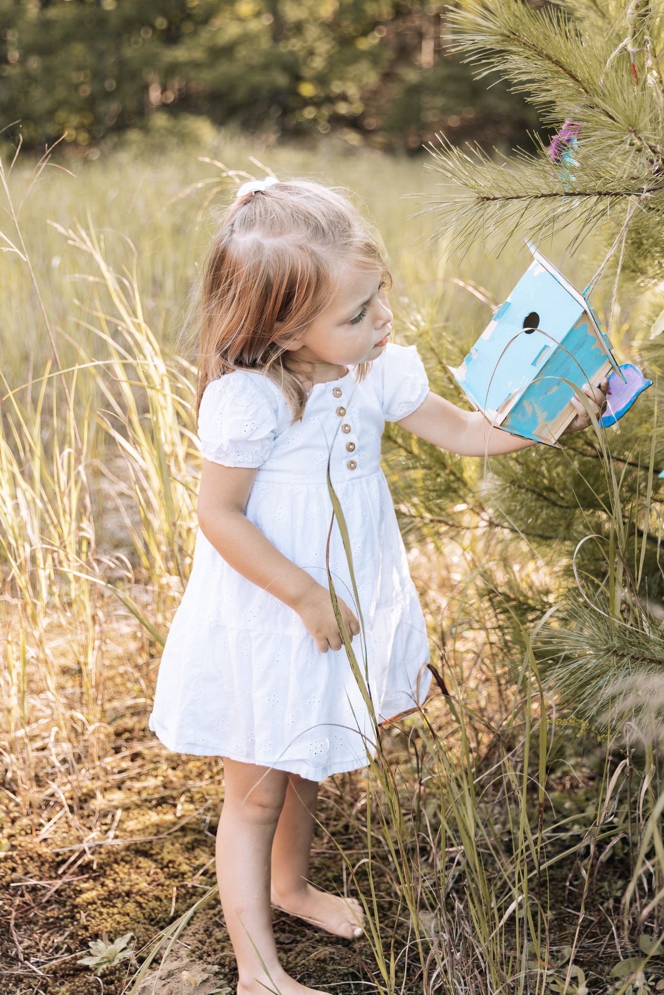 A small child in white dress explores tall grass and wildflowers in golden sunlight.