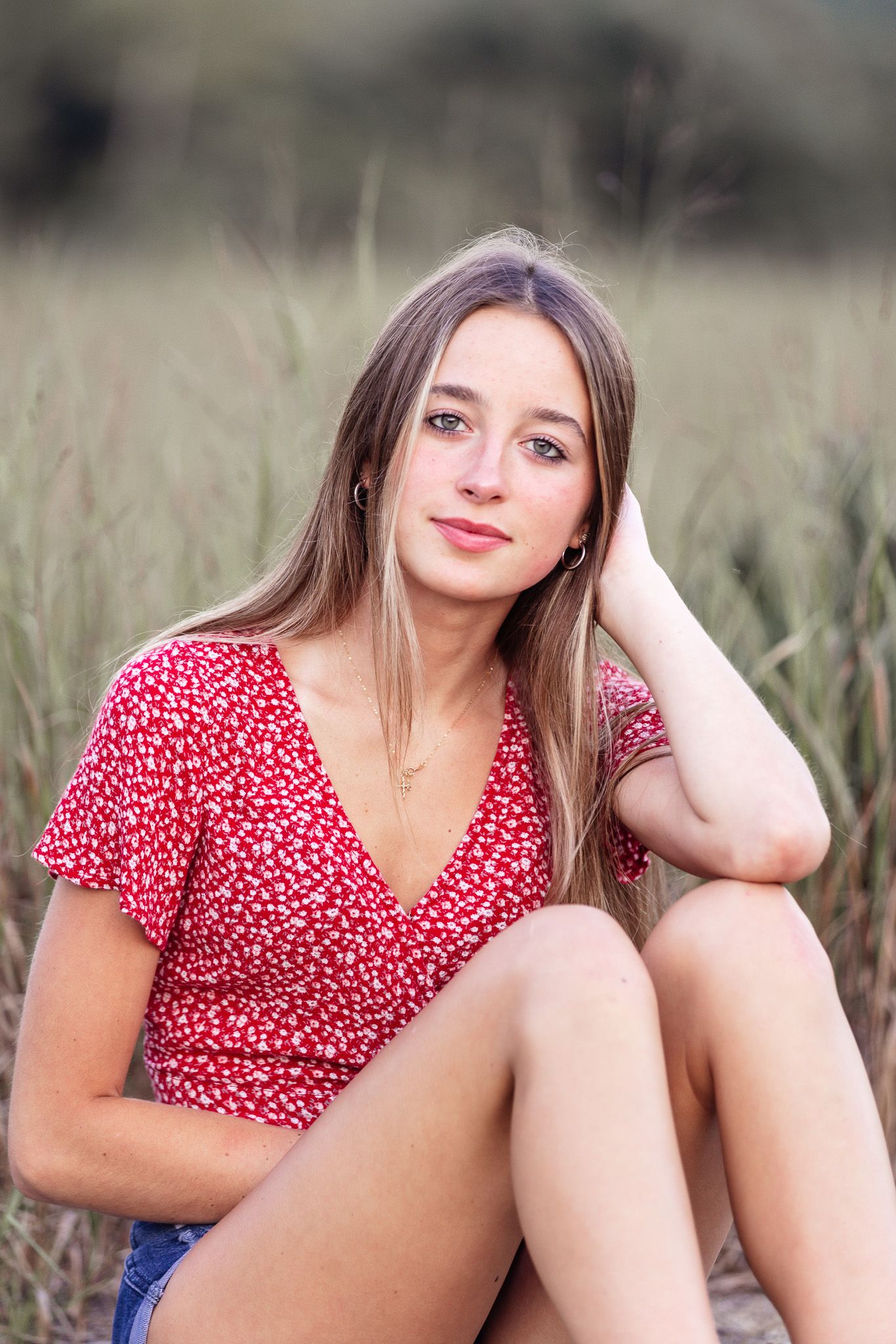 Person wearing red polka dot dress poses in field during outdoor portrait session.