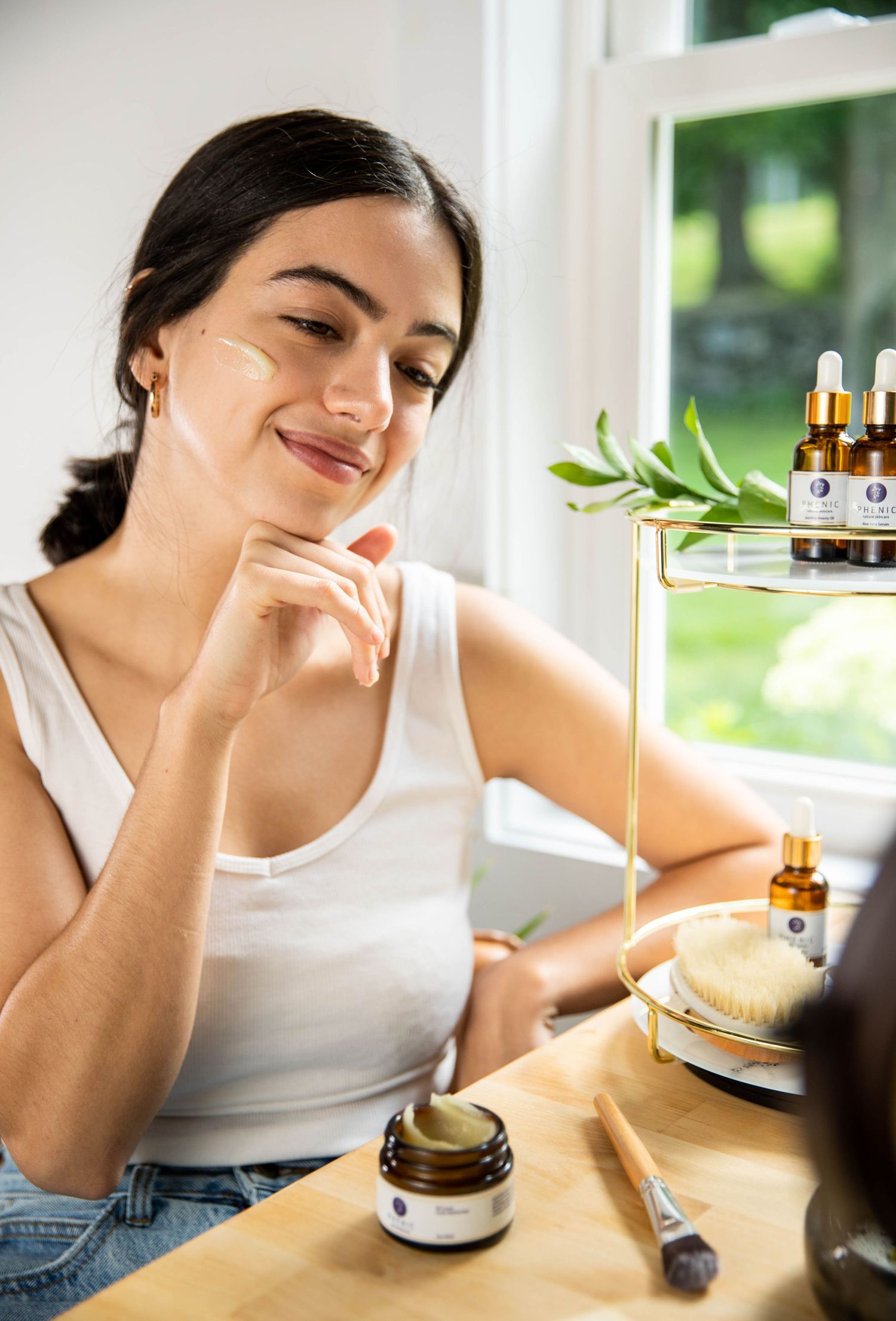 Person examining skincare products at wooden table near window.
