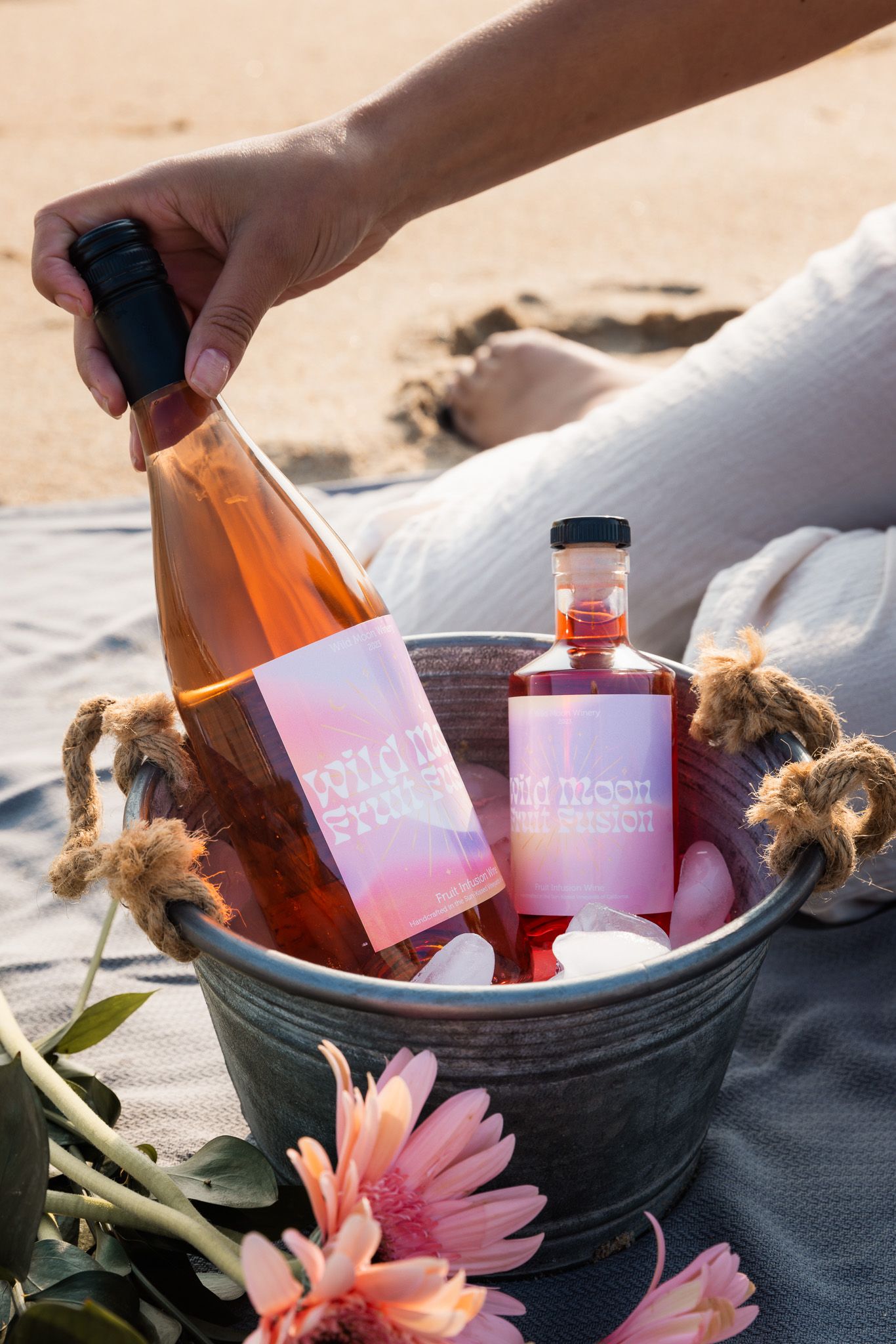 Pink and orange beverage bottles arranged in an ice bucket with flowers for a summer picnic.