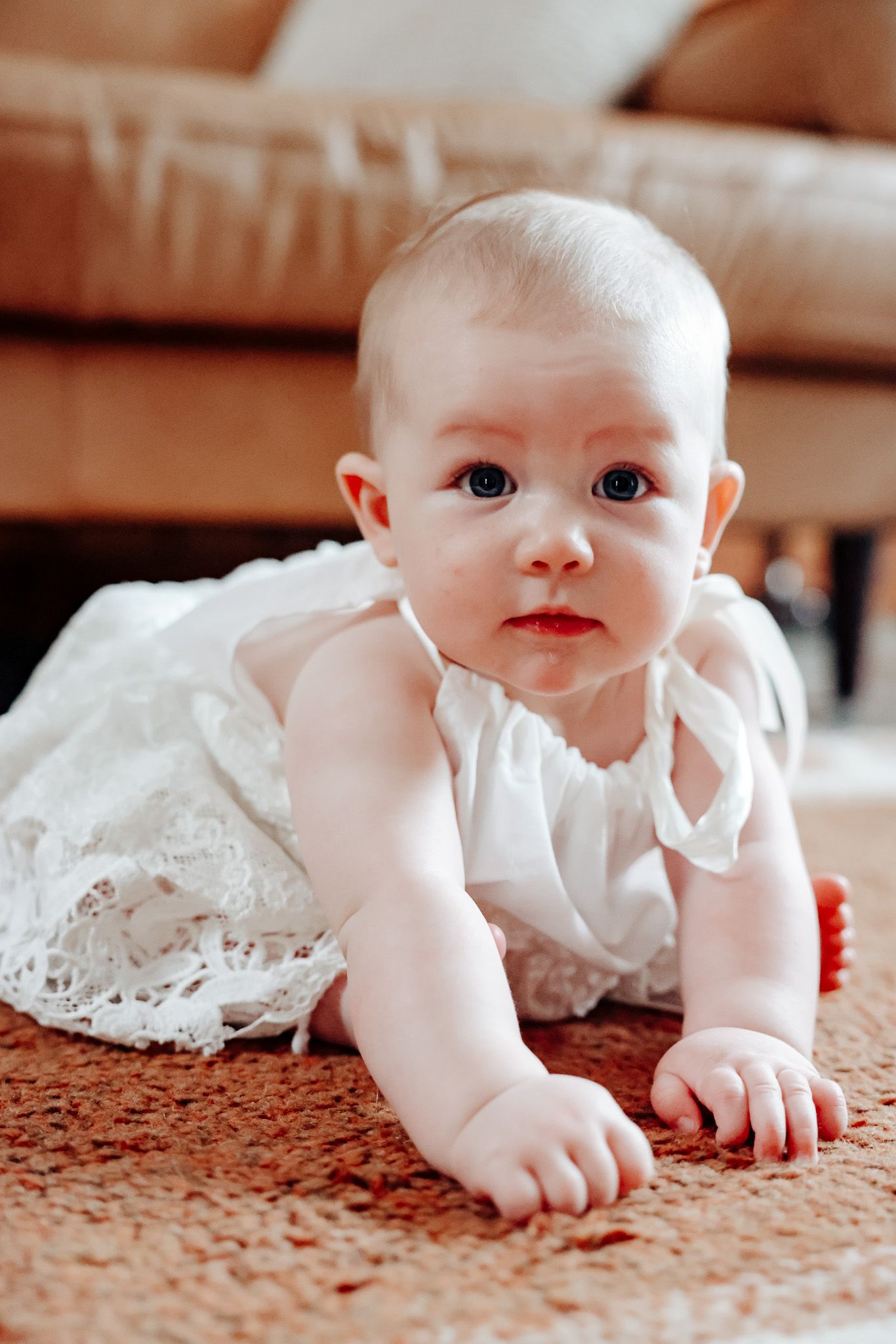 Baby in white lace dress crawling on carpet.