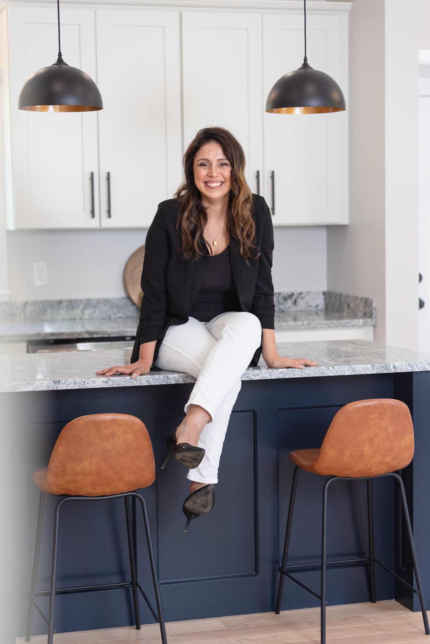 Modern kitchen featuring navy blue island, pendant lights, and cognac leather barstools.