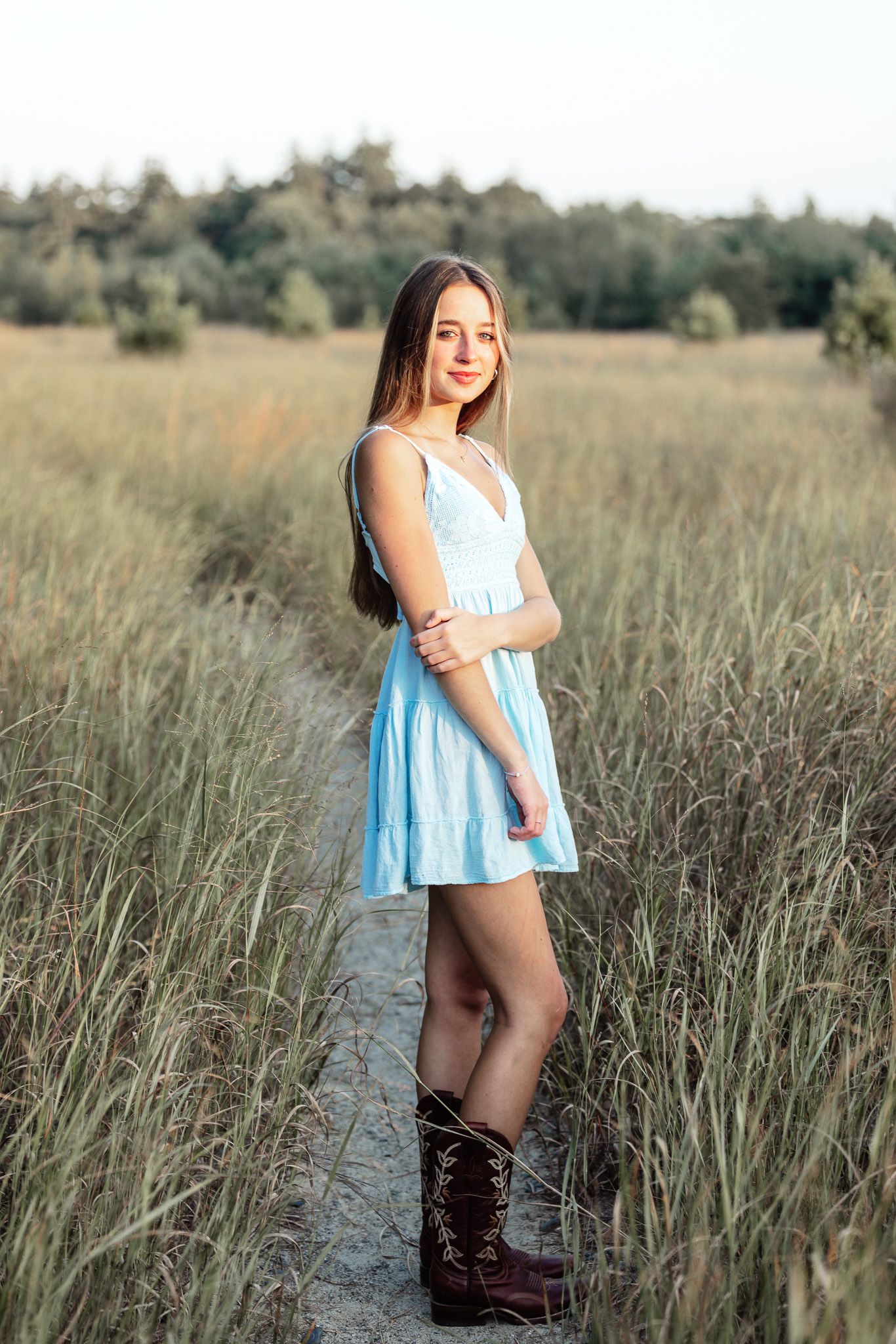 Person in flowing blue dress stands in rustic field setting during portrait session.