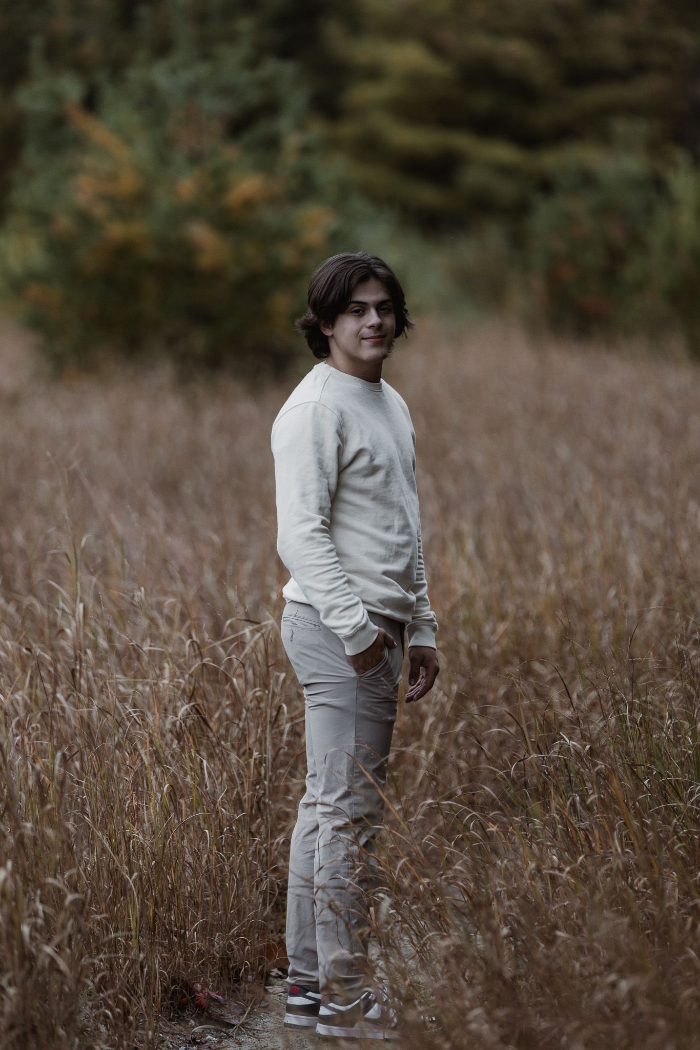 Figure in monochromatic white outfit poses naturally in field of dried winter grass.