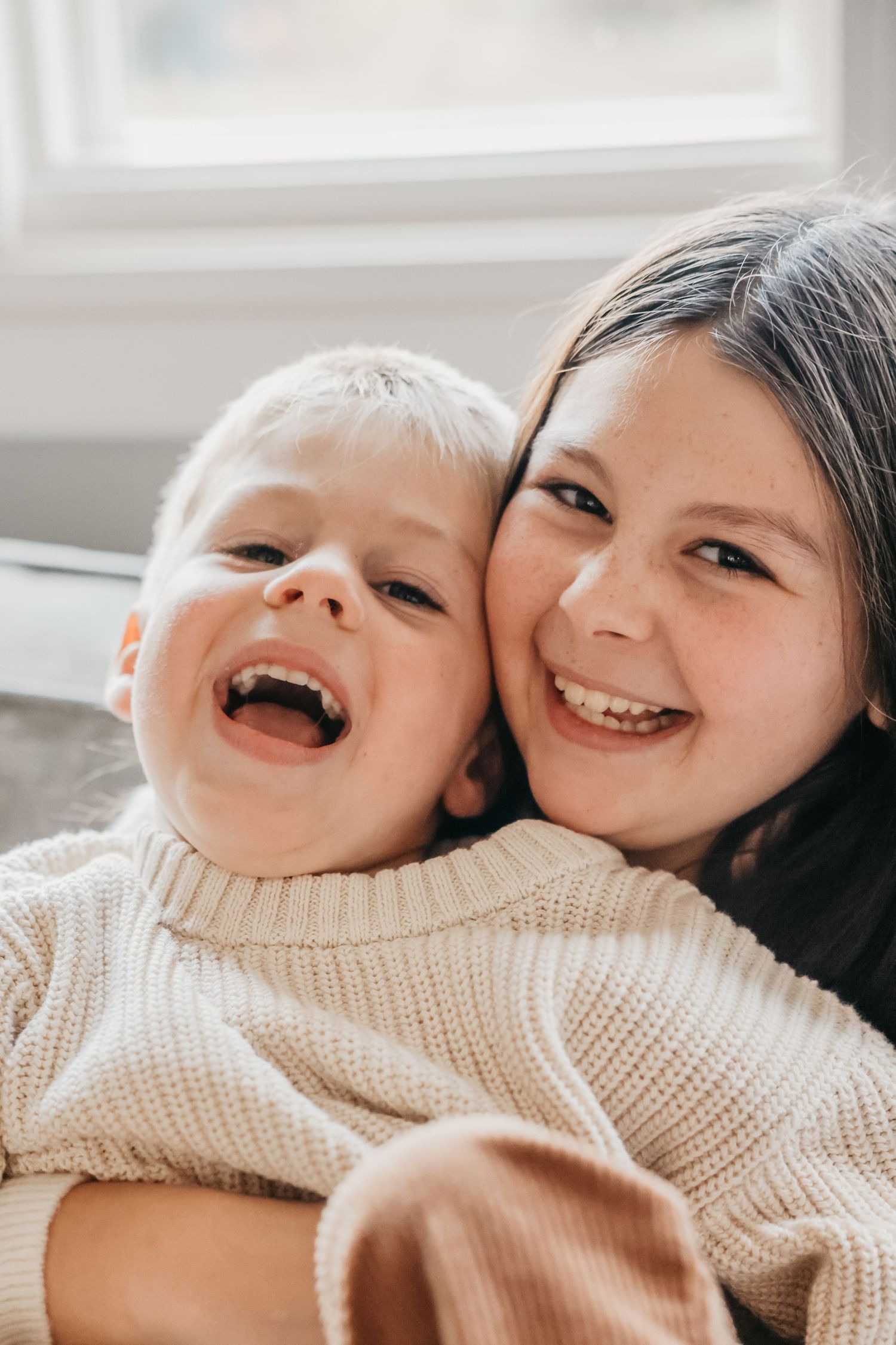 Cozy indoor portrait showing genuine laughter and joy in cream sweaters.