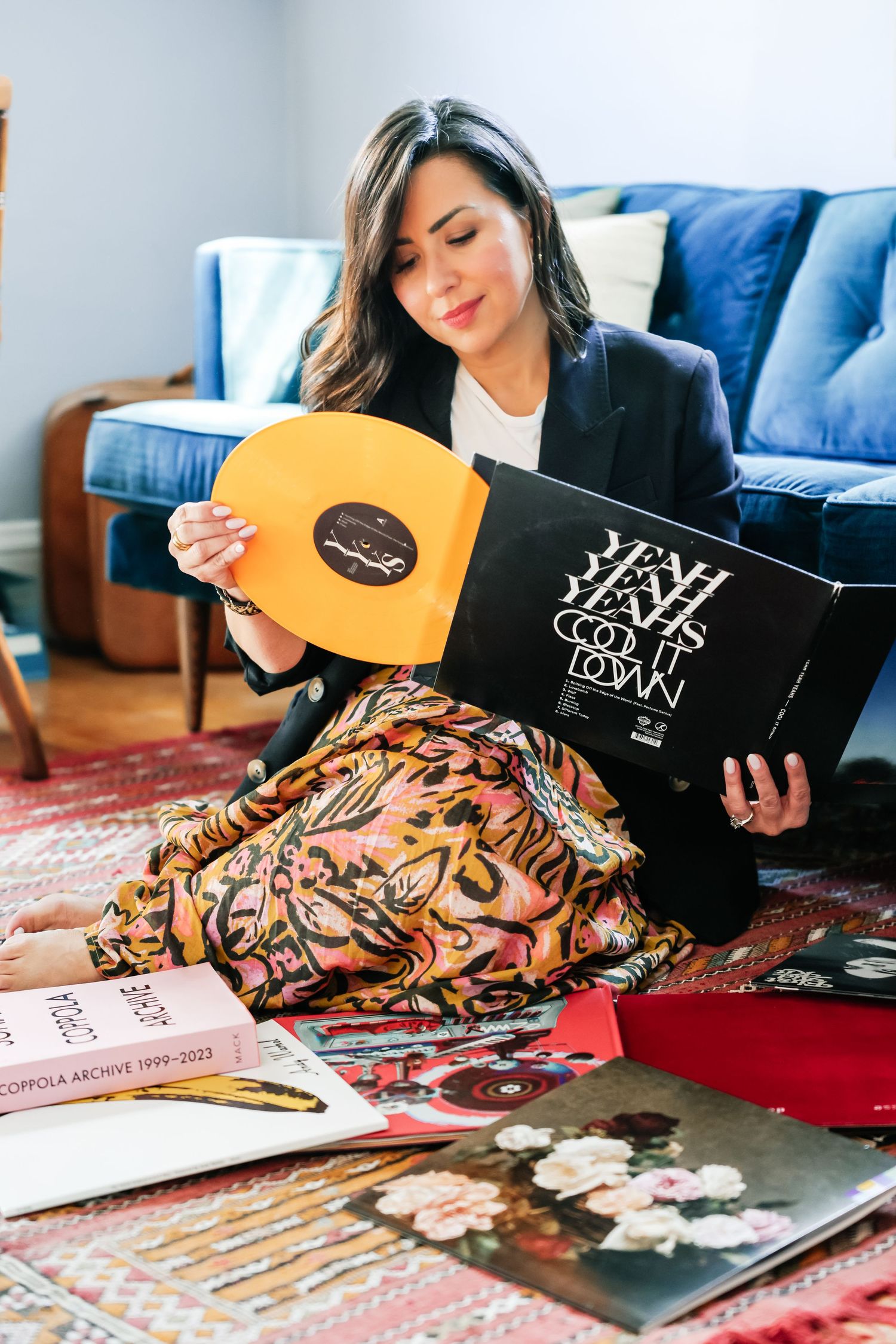 Woman sitting on floor examining colorful vinyl records, surrounded by album covers and a floral skirt.