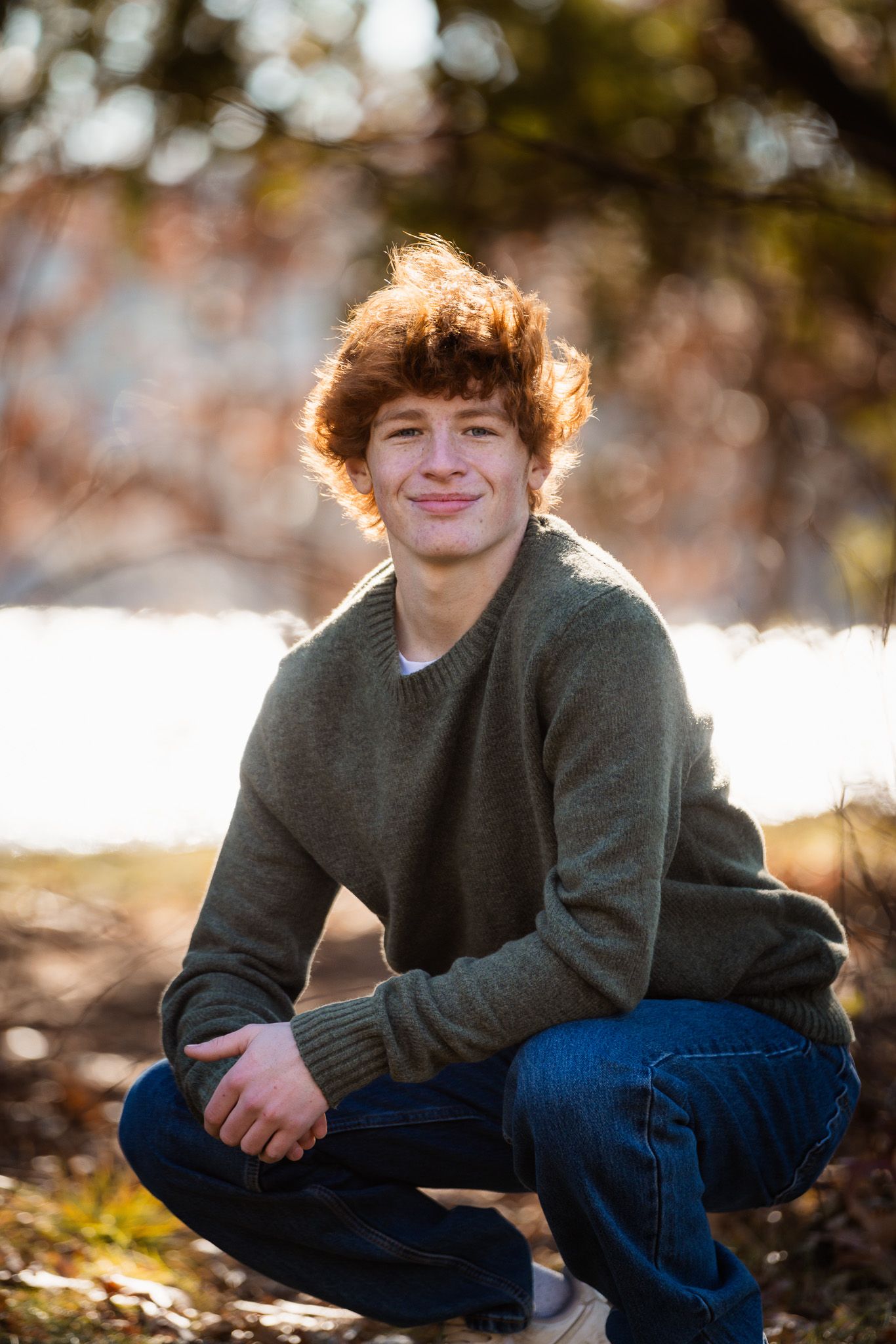 Candid outdoor photo showing relaxed pose on ground with autumn foliage in background.