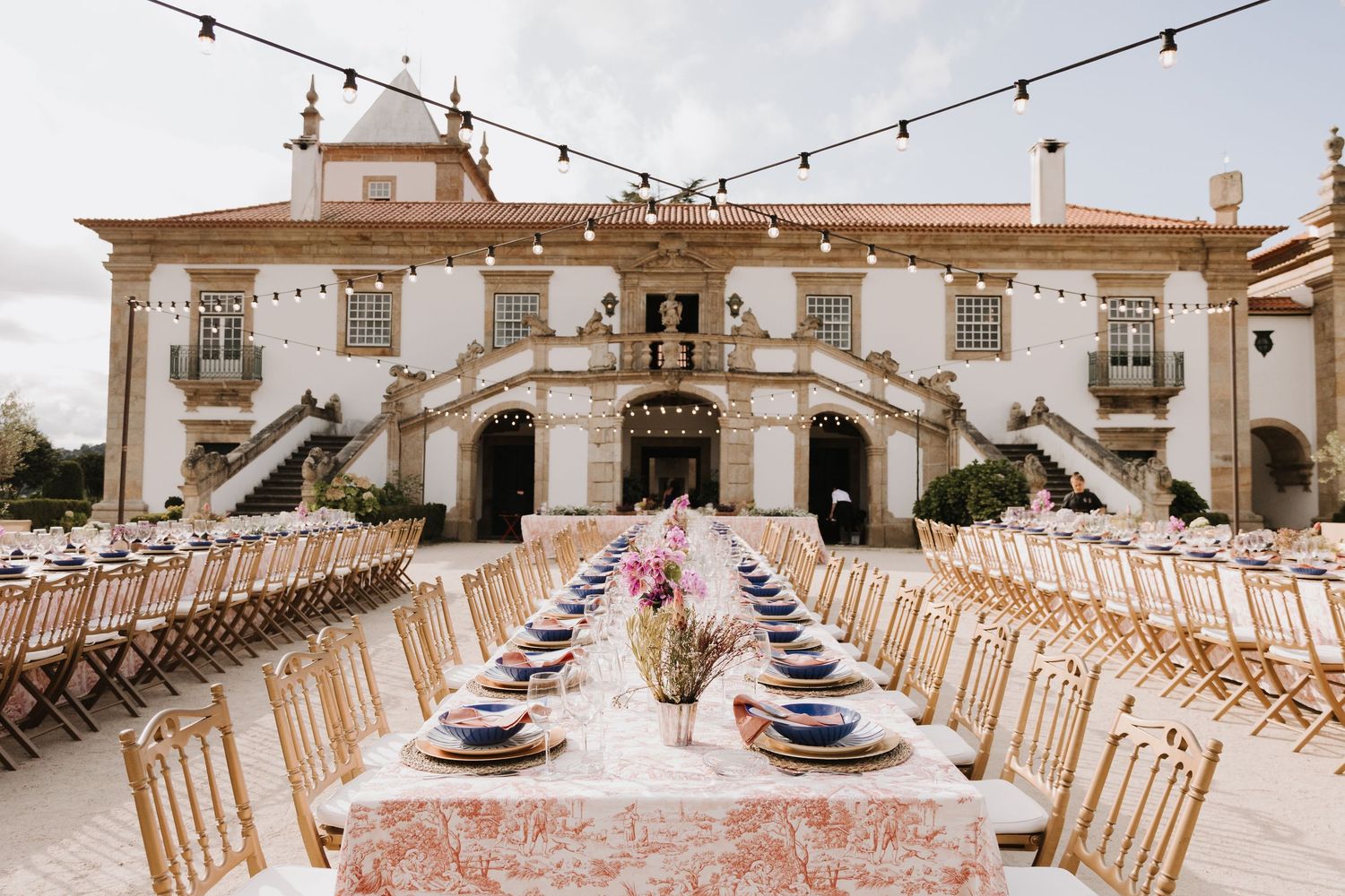 Elegant outdoor wedding reception with long decorated tables set in front of a grand historic mansion.