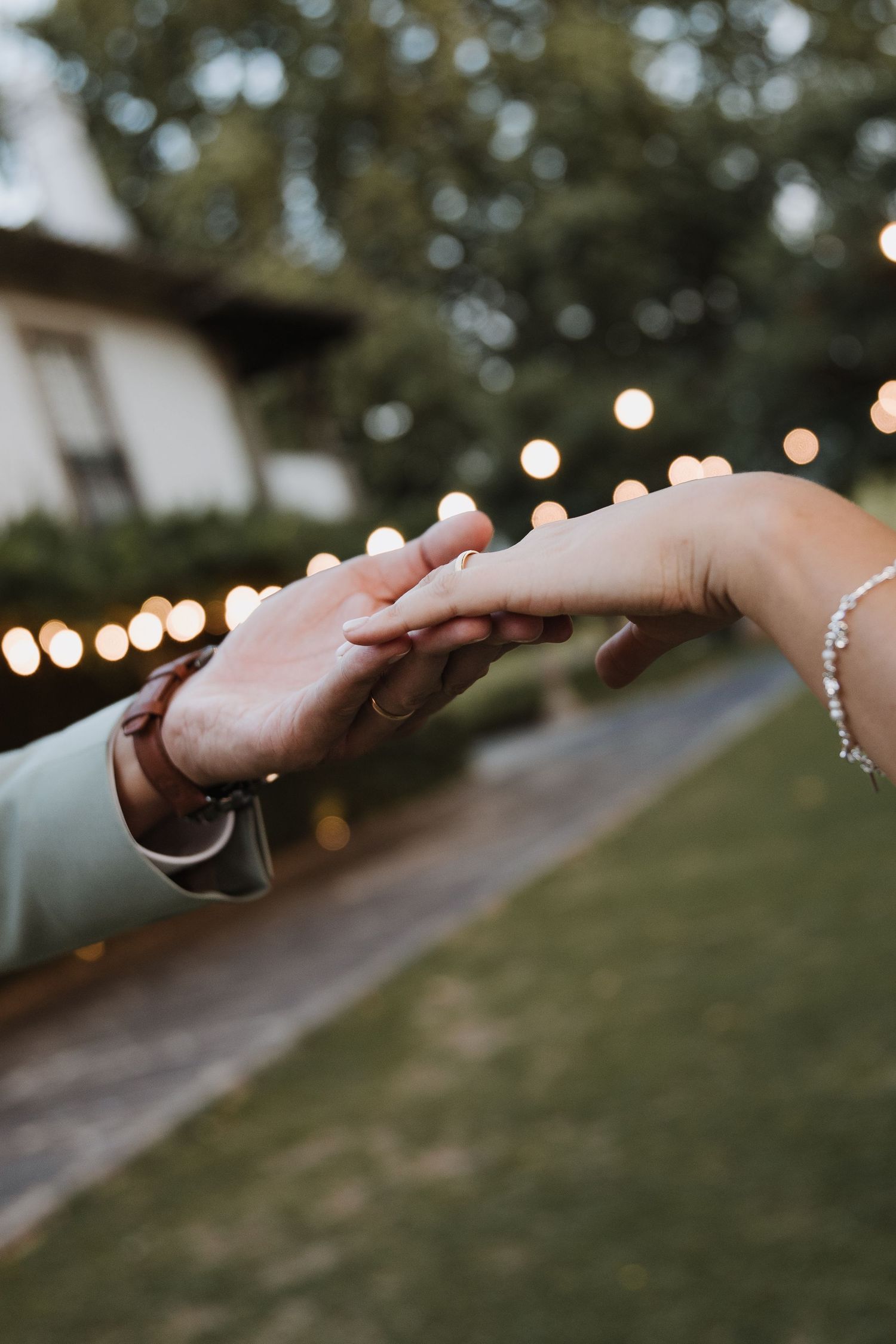 Close-up of a couple holding hands, bride wearing diamond bracelet and engagement ring at outdoor wedding.