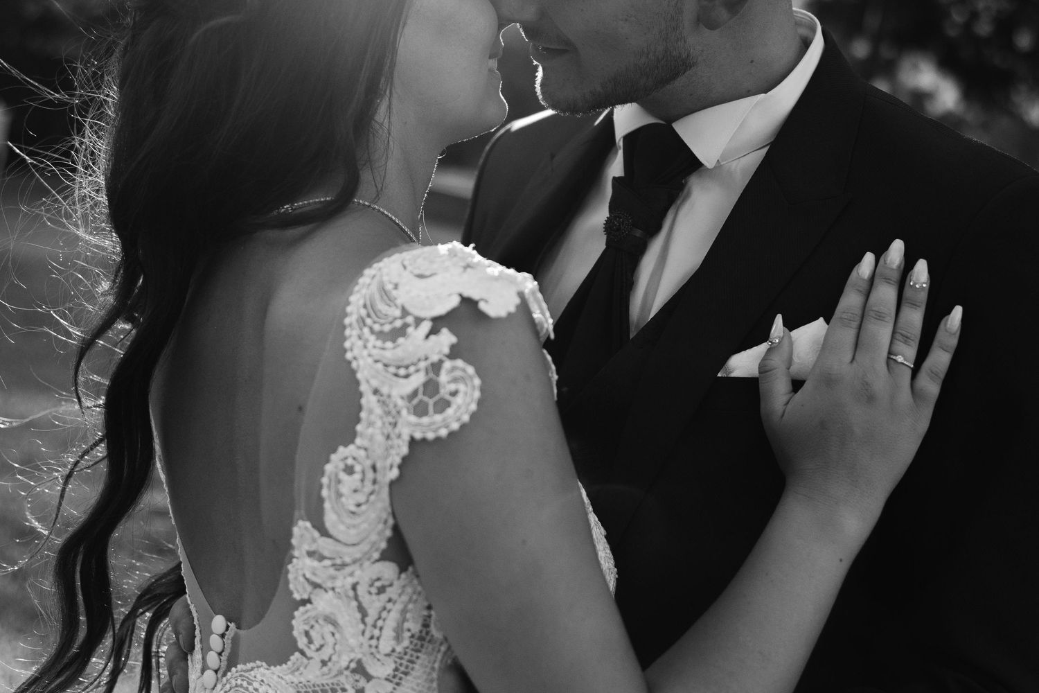 Close-up black and white photo of a bride and groom nearly kissing, highlighting lace wedding dress detail.