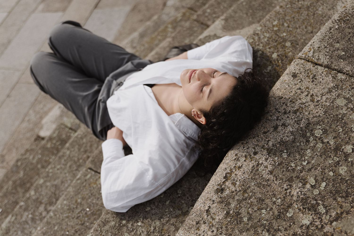 Person in white shirt lying relaxed on stone steps with eyes closed outdoors.