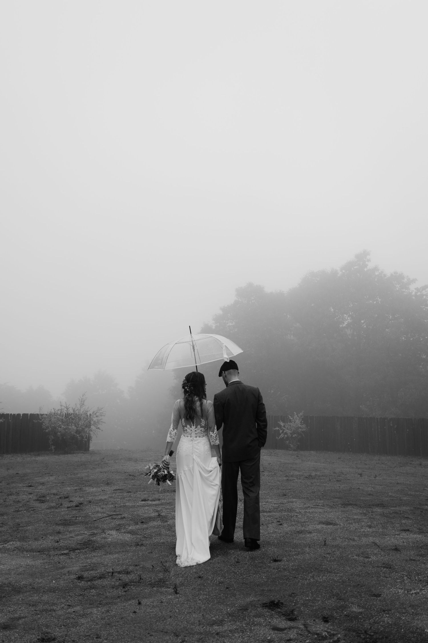Bride and groom standing together under a white umbrella in a misty foggy landscape in black and white.