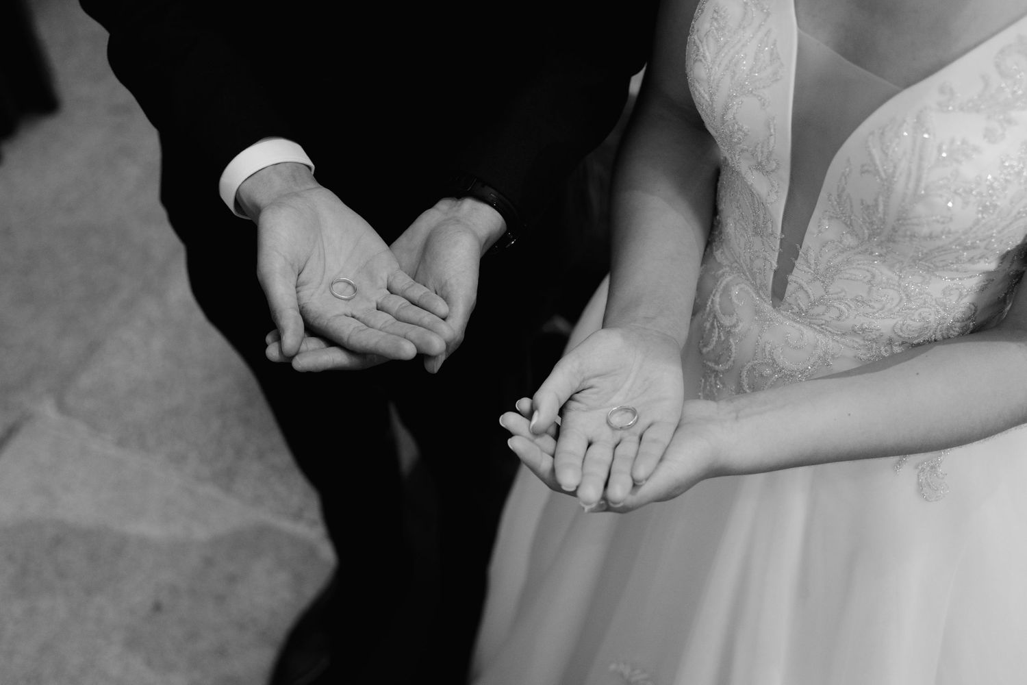 Bride and groom displaying wedding rings in their open palms in black and white close-up photo.