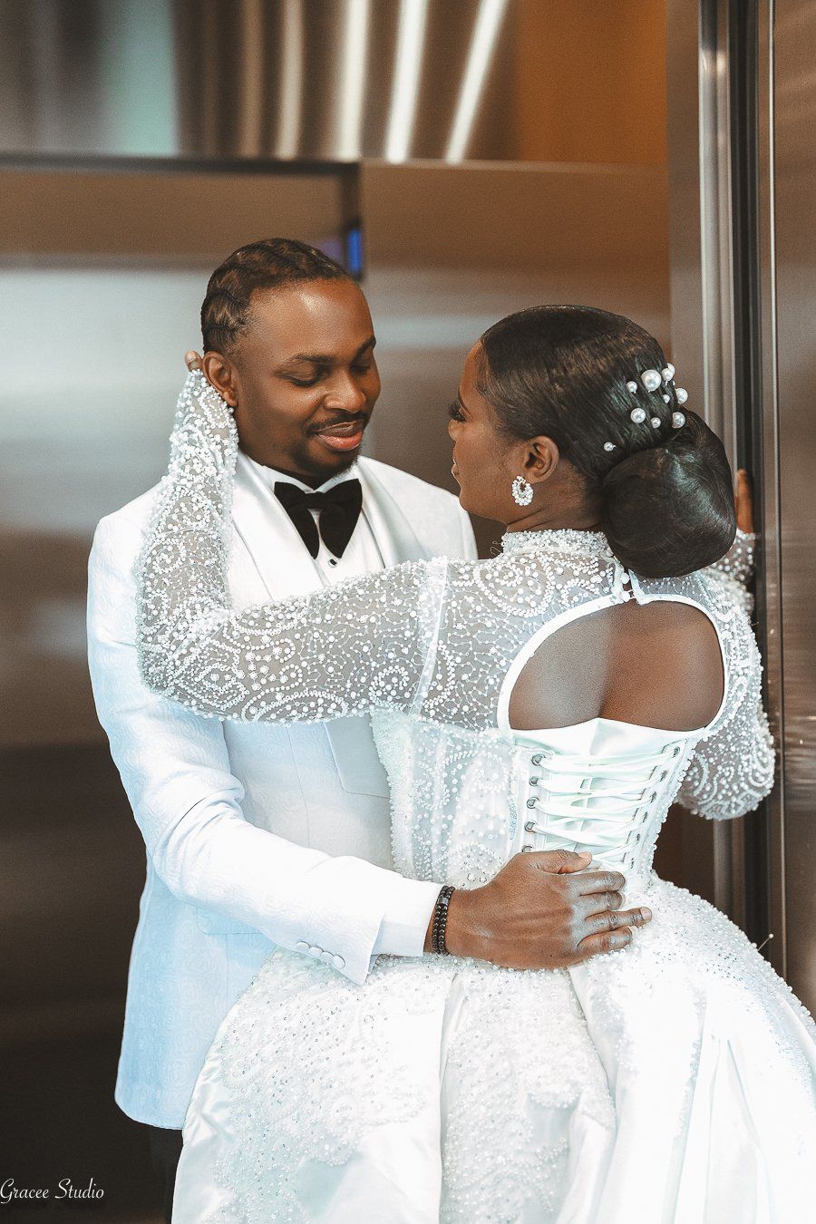 A bride and groom share an intimate moment in formal white wedding attire during their celebration.