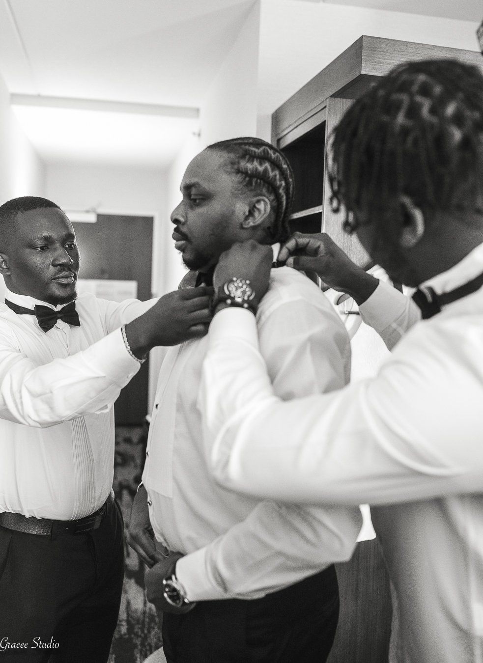 Groomsmen in white shirts helping the groom with his wedding outfit.