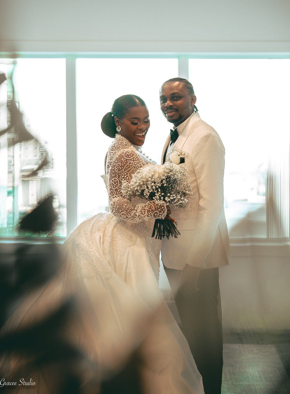 A couple in elegant white attire shares an intimate moment during their wedding celebration in a bright indoor venue.